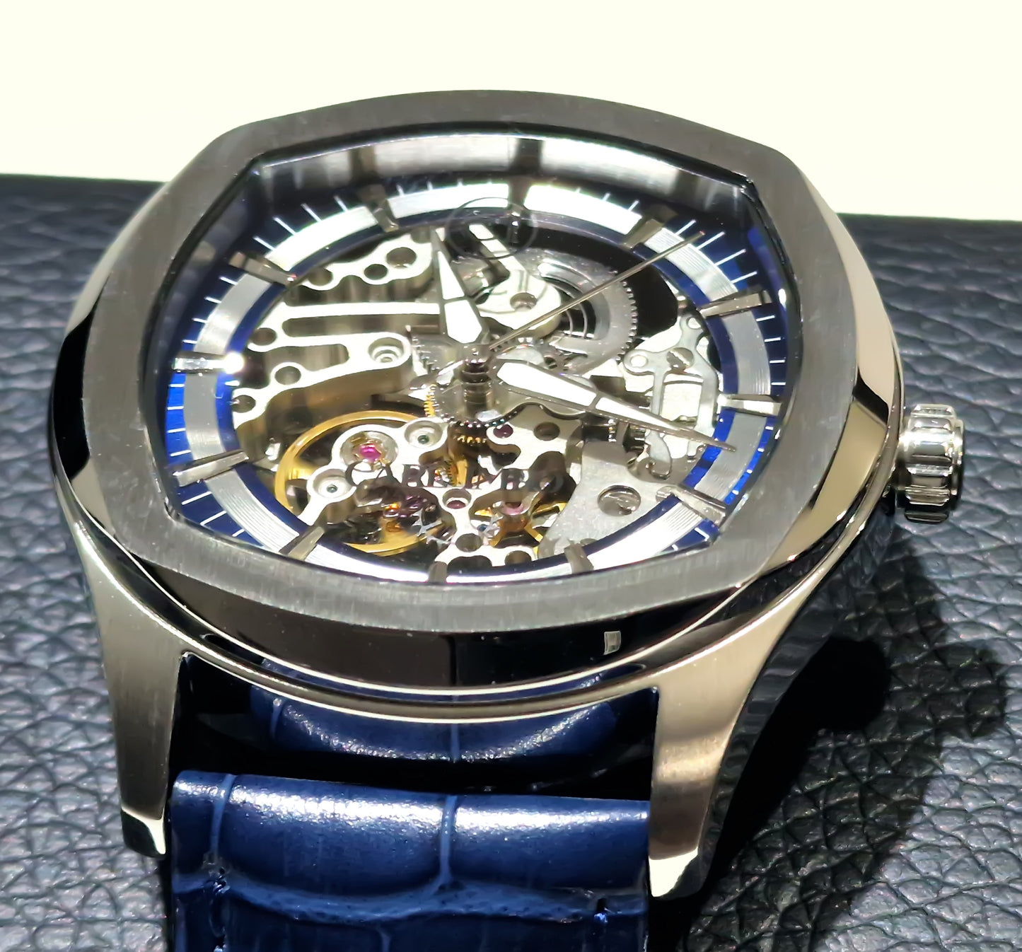 Montre squelette cadran rond: mécanisme doré avec anneaux bleus, boîtier acier.