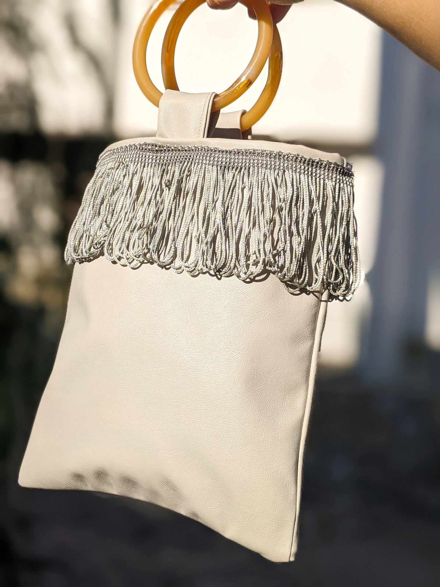 Sac mini simili cuir gris clair, anse anneau orange, franges sur bande supérieure.