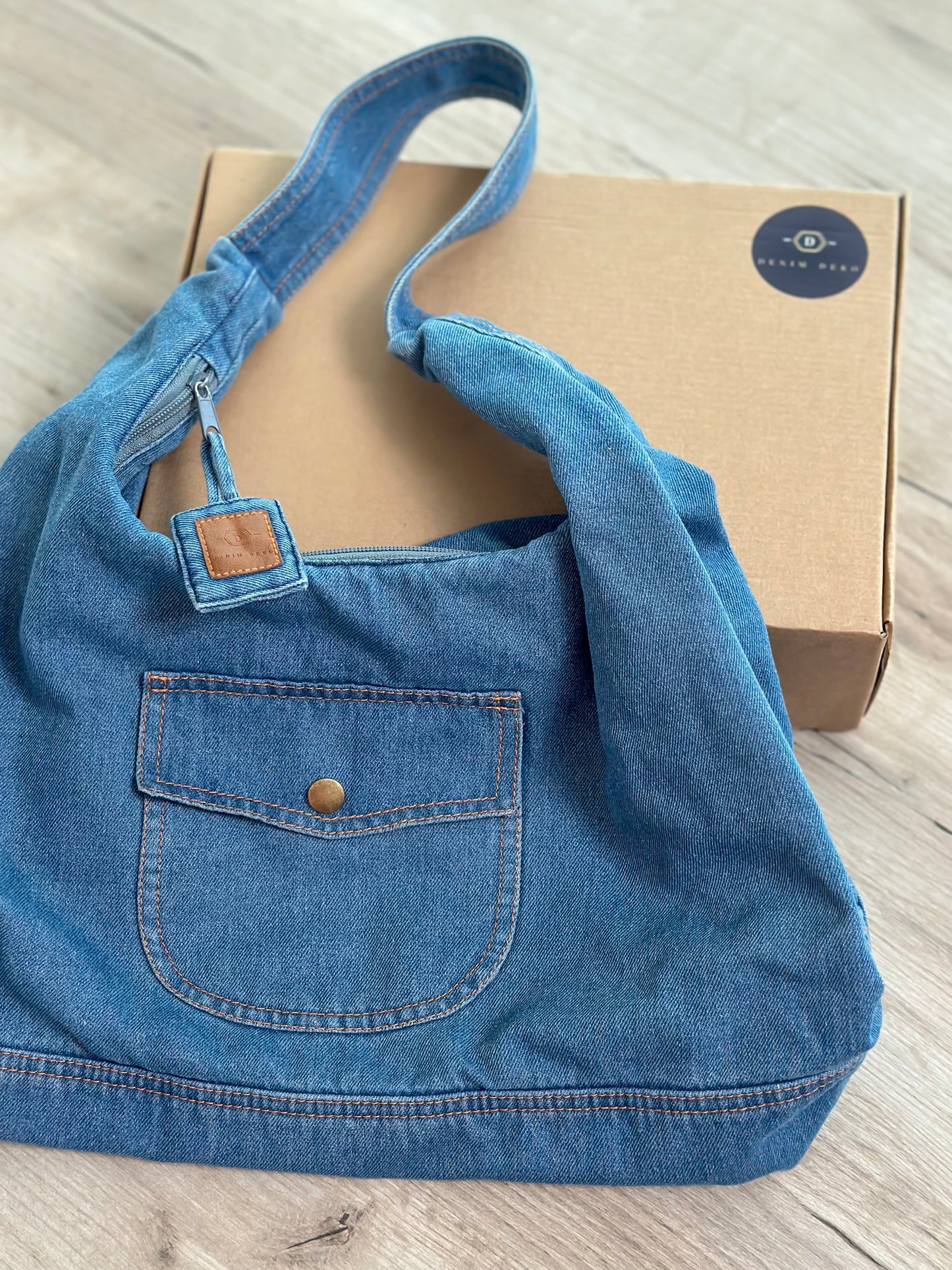 Sac hobo en jean bleu clair, anses longues et poche plaquée avec bouton.