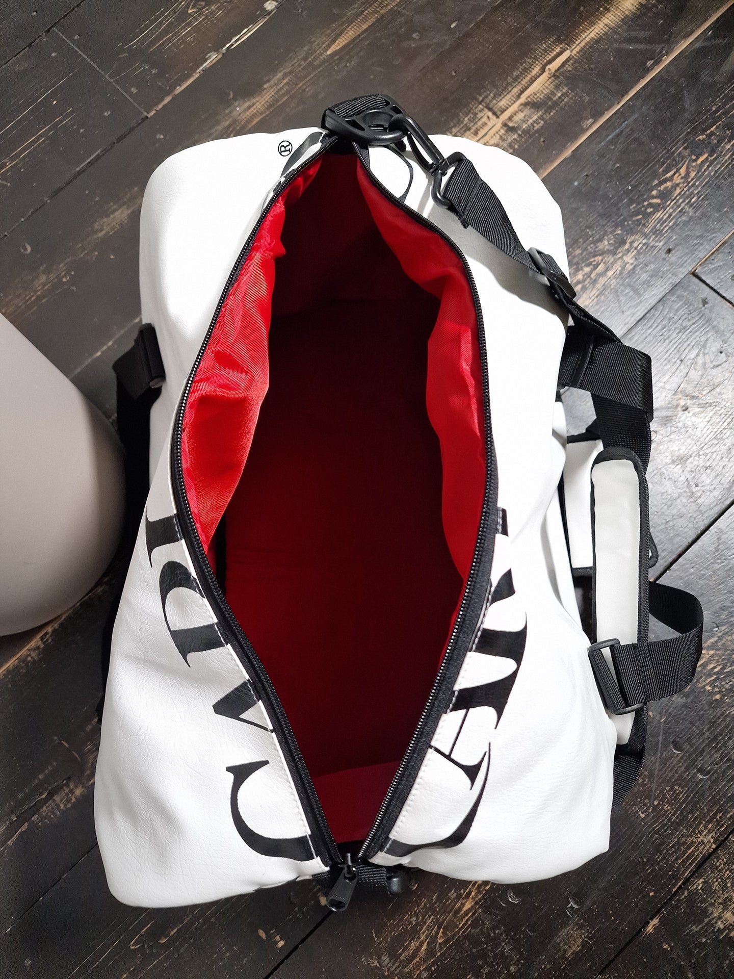 Sac en cuir blanc avec bandoulière noire; intérieur rouge visible et fermeture zippée.