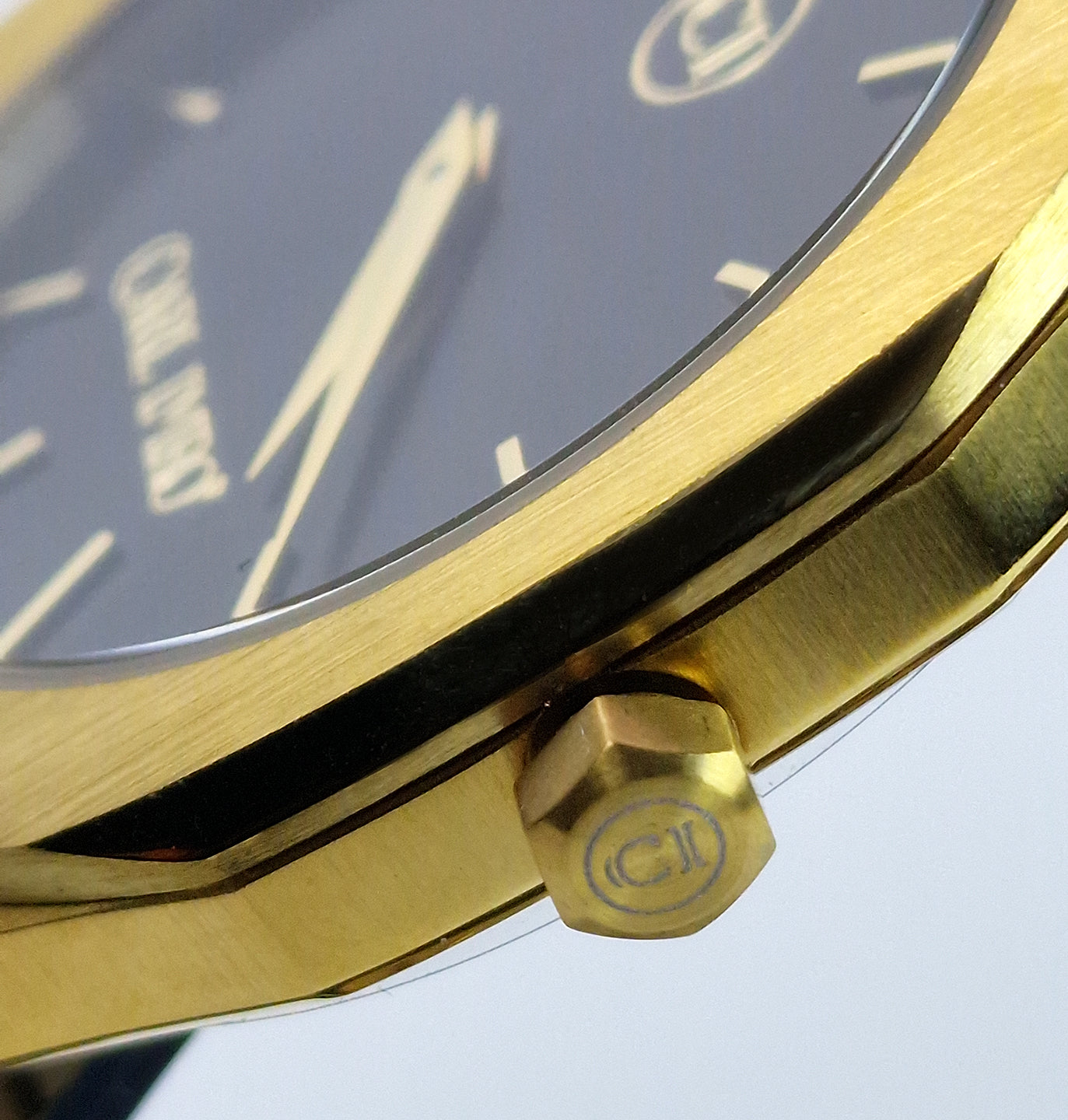 Couronne de montre acier doré avec logo circulaire.