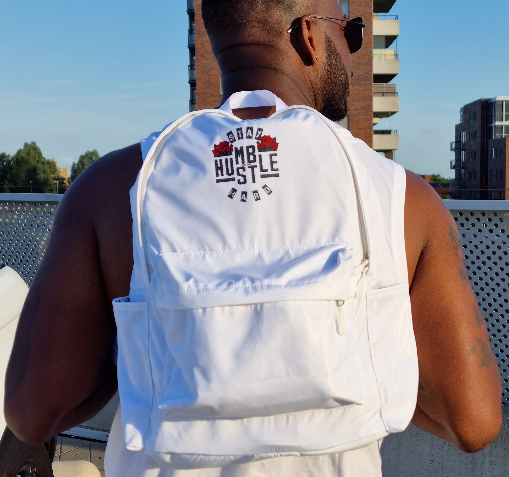Sac à dos blanc porté devant, logo « Hustle Hard » et bretelles réglables