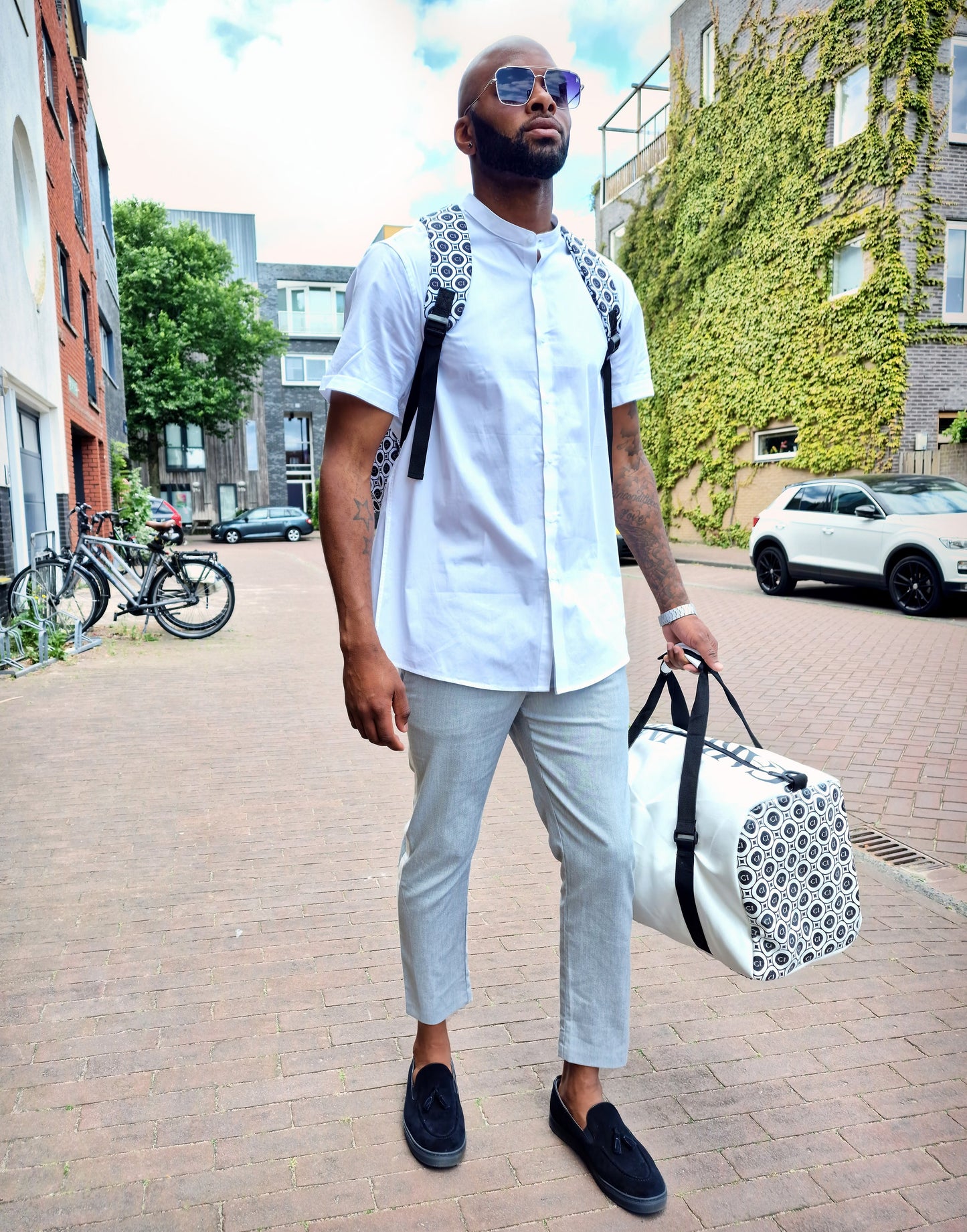 Sac en cuir blanc à bandoulière noire, motifs de cercles gris et poignée supérieure.