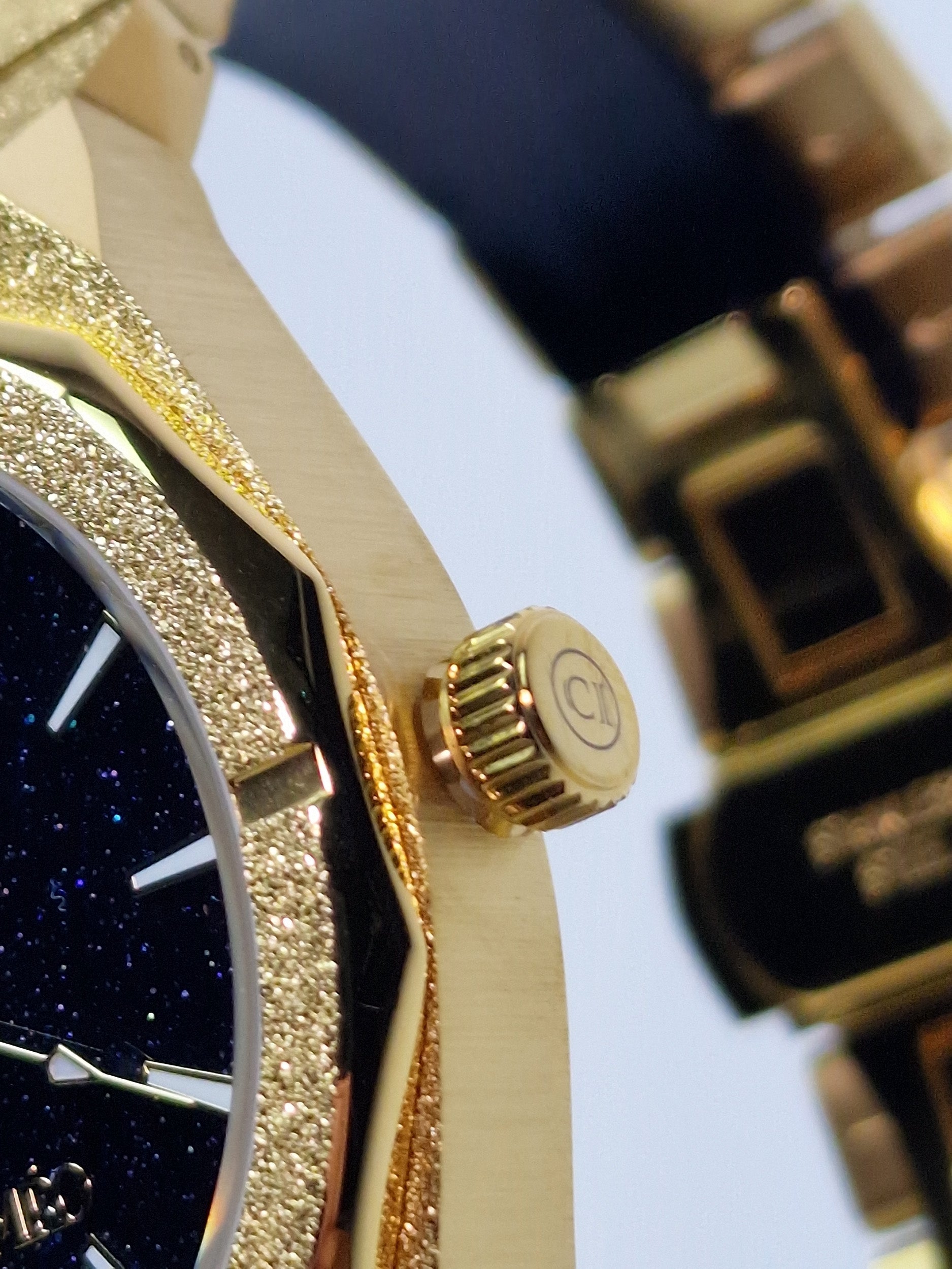 Montre homme, couronne dorée striée et lunette strass autour du cadran bleu.