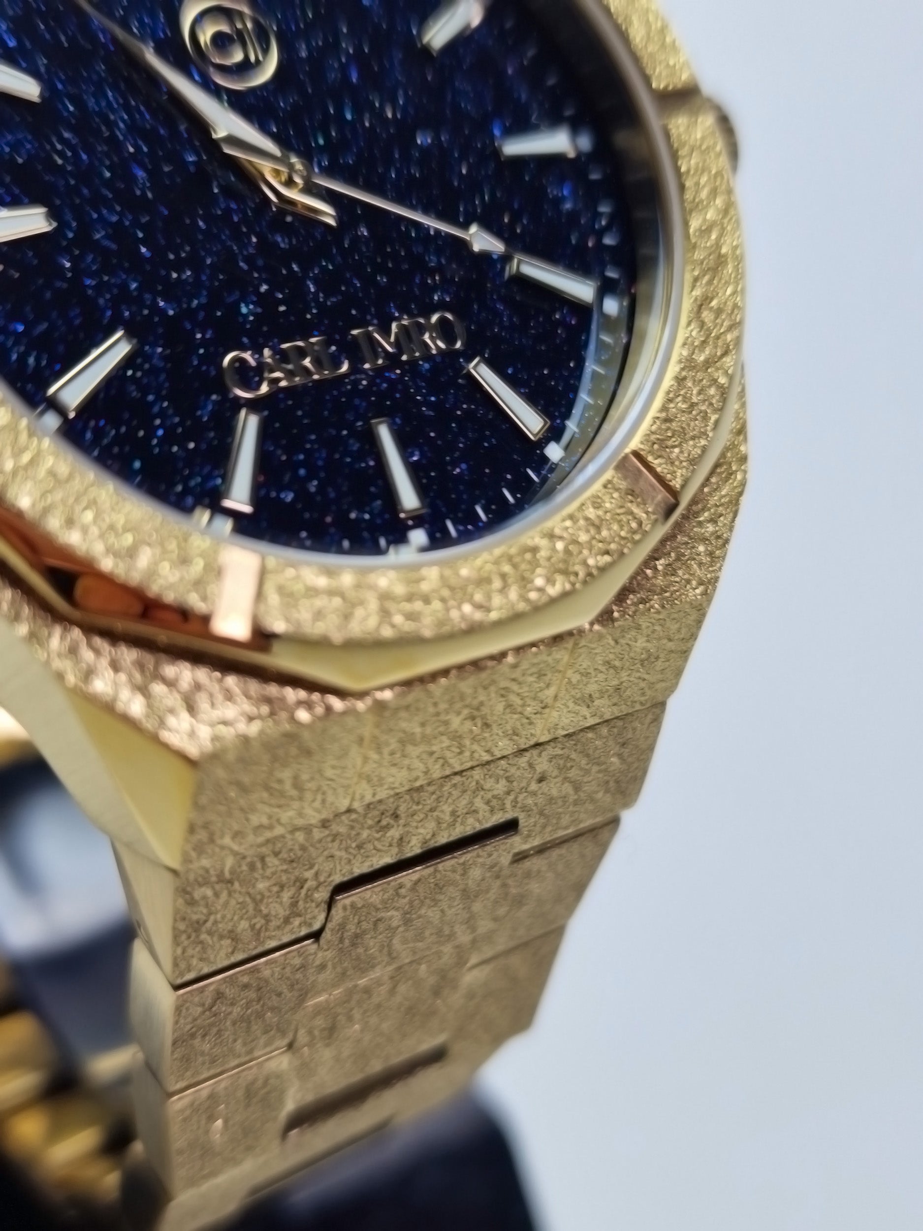 Montre homme, lunette strass dorée et cadran bleu nuit; maillons rectangulaires gravés.