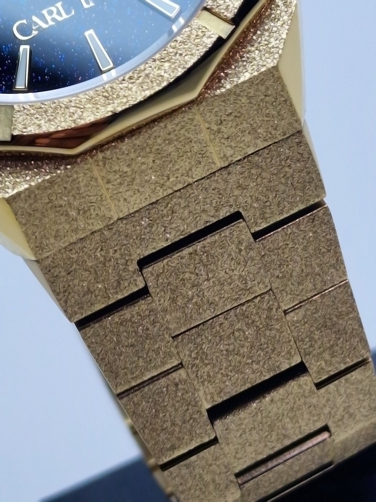 Montre homme, bracelet acier doré avec maillons gravés et texture grainée.