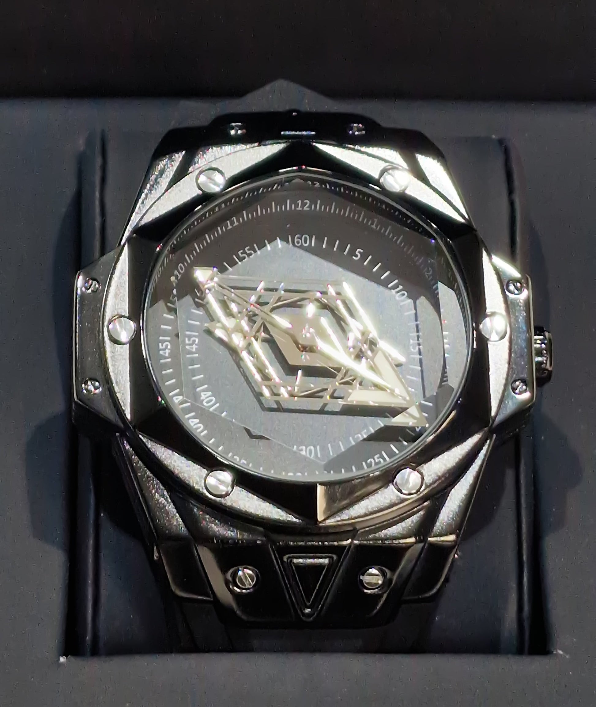 Montre homme dans un écrin, cadran noir brillant et boîtier argenté avec détails.