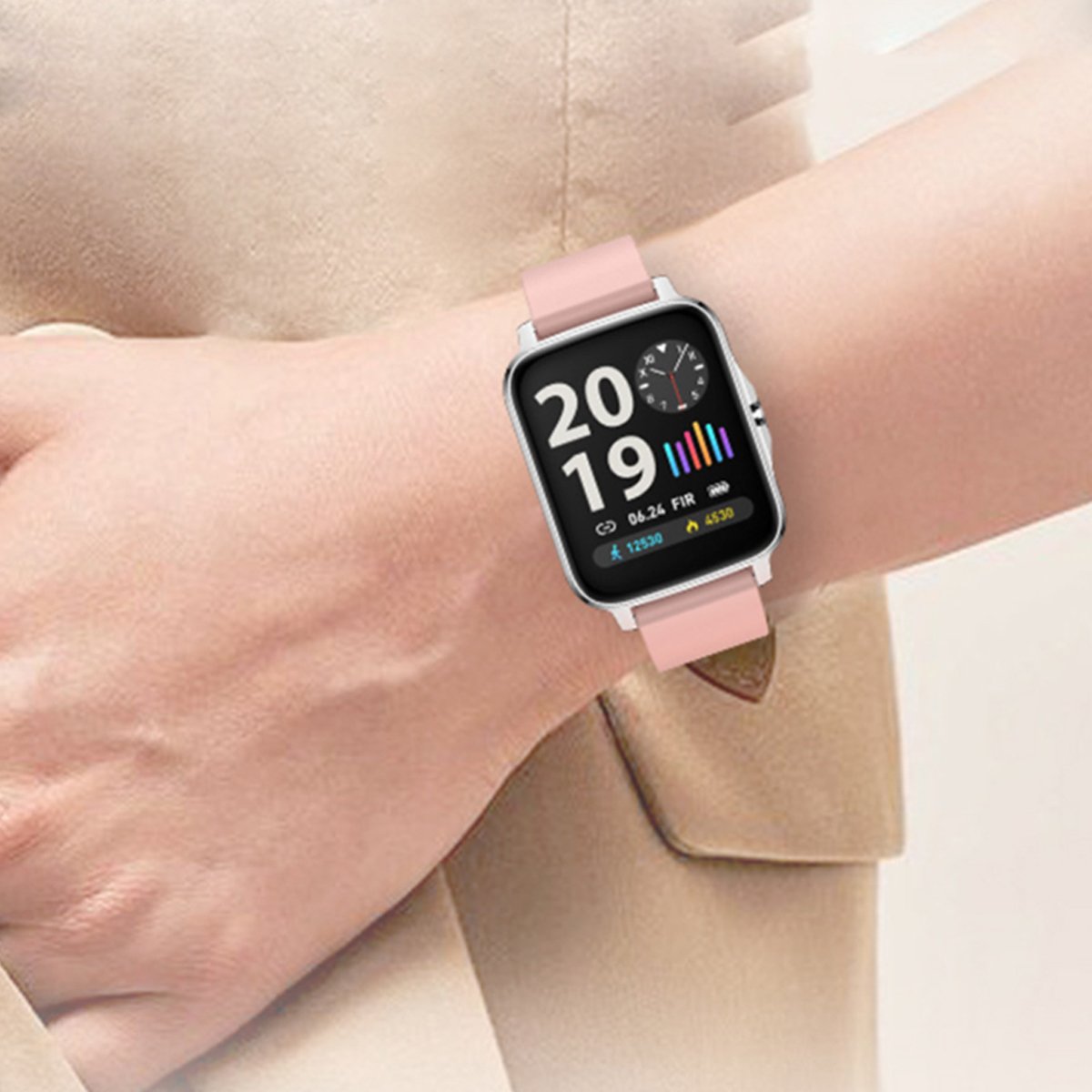 Montre connectée portée: boîtier noir, bracelet rose clair, cadran avec indicateurs.