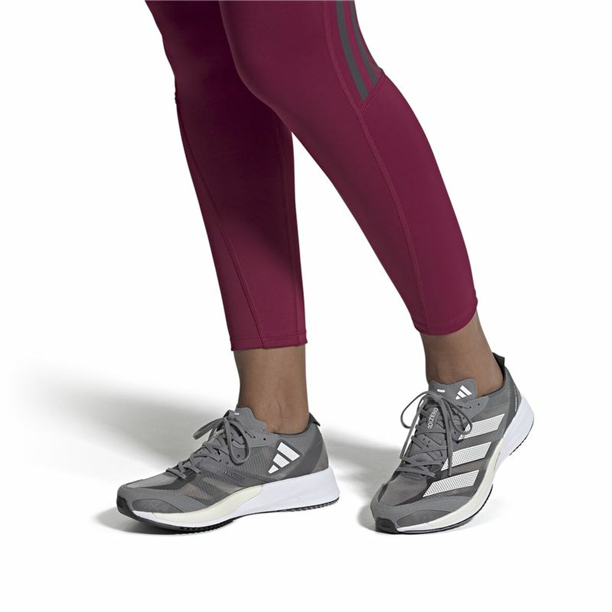 Chaussure adidas grise foncée avec laçage, sur pantalon bordeaux, semelle blanche