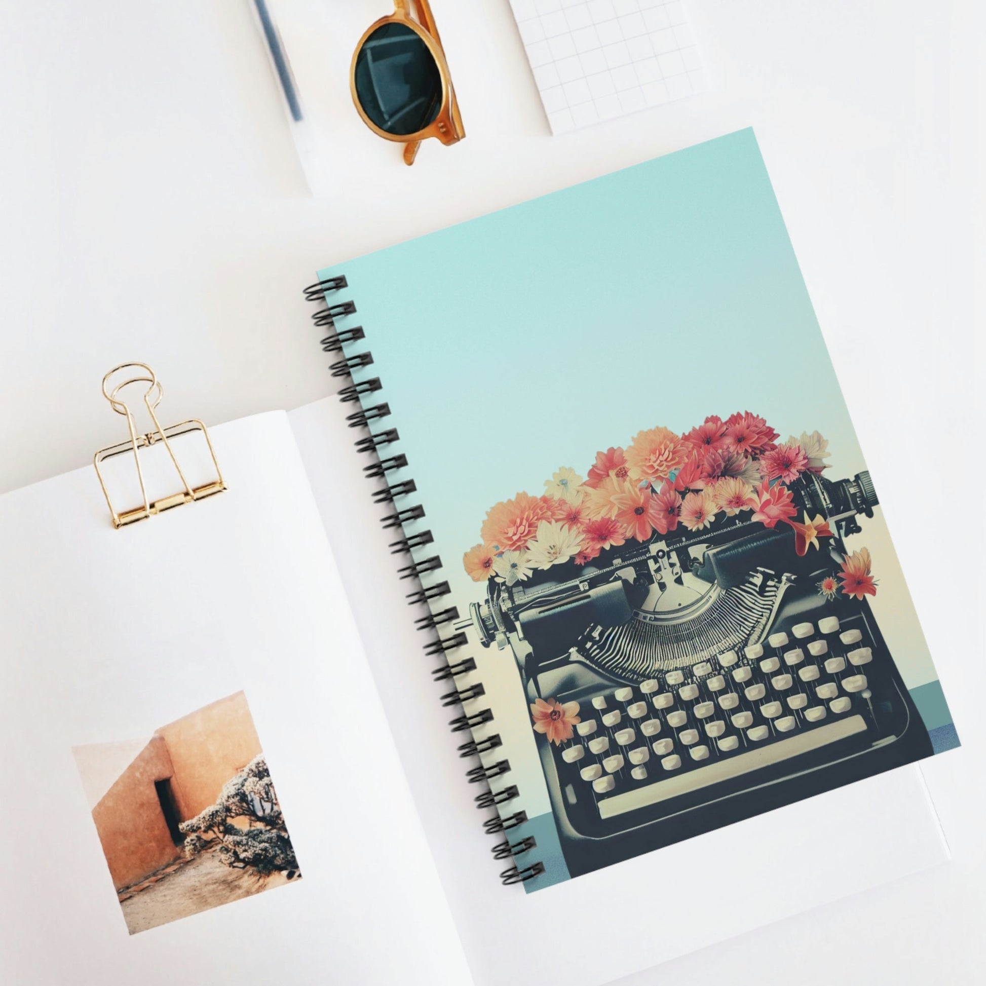 Carnet spiralé illustré bleu menthe : machine à écrire noire entourée de fleurs multicolores