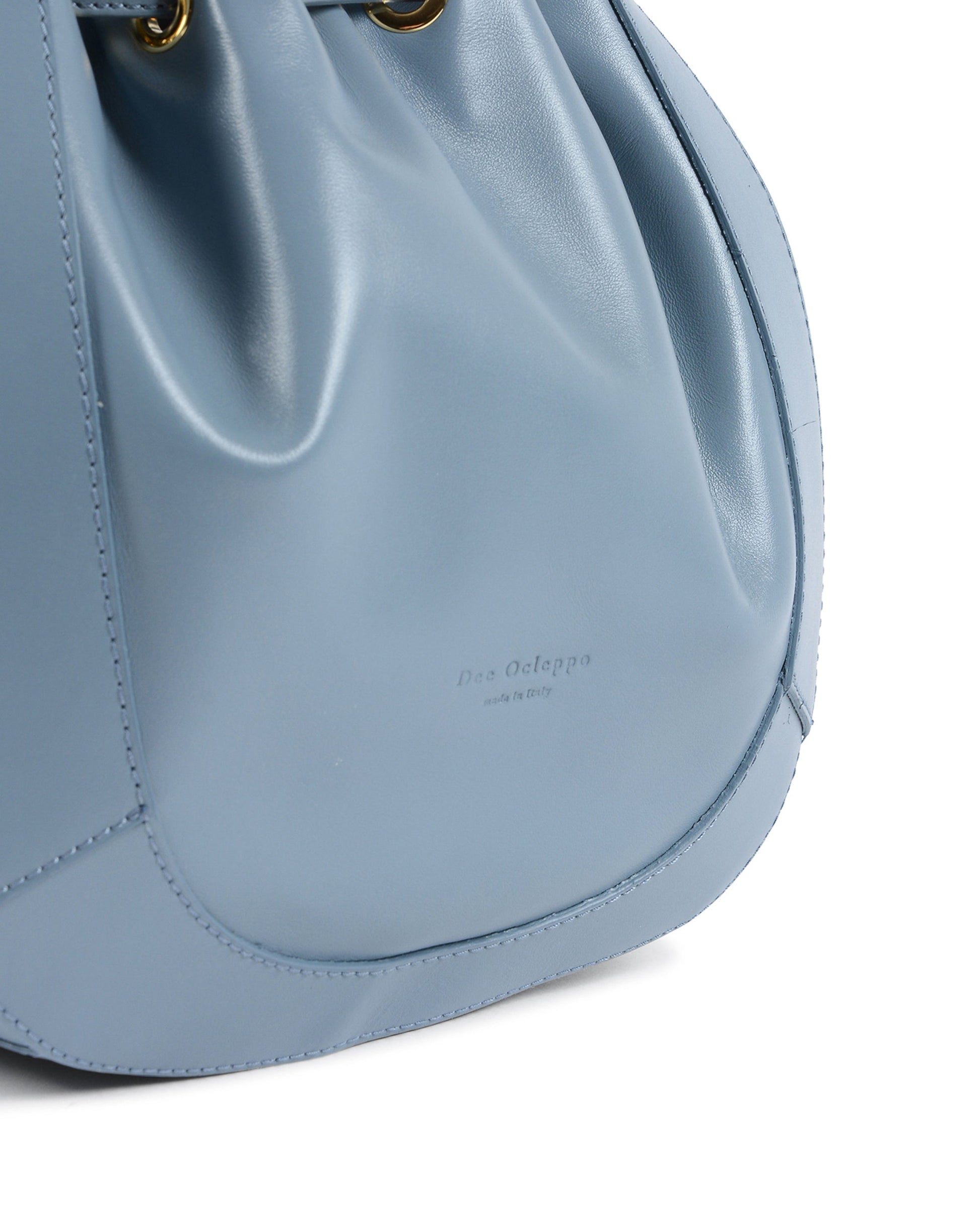 Sac seau bleu clair, détail du cuir et du bas arrondi, couture visible.