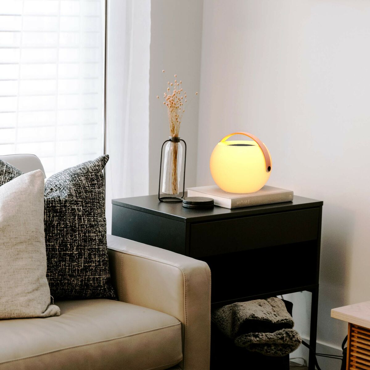 Enceinte Bluetooth portable ronde à lumière jaune, poignée visible, posée sur table.
