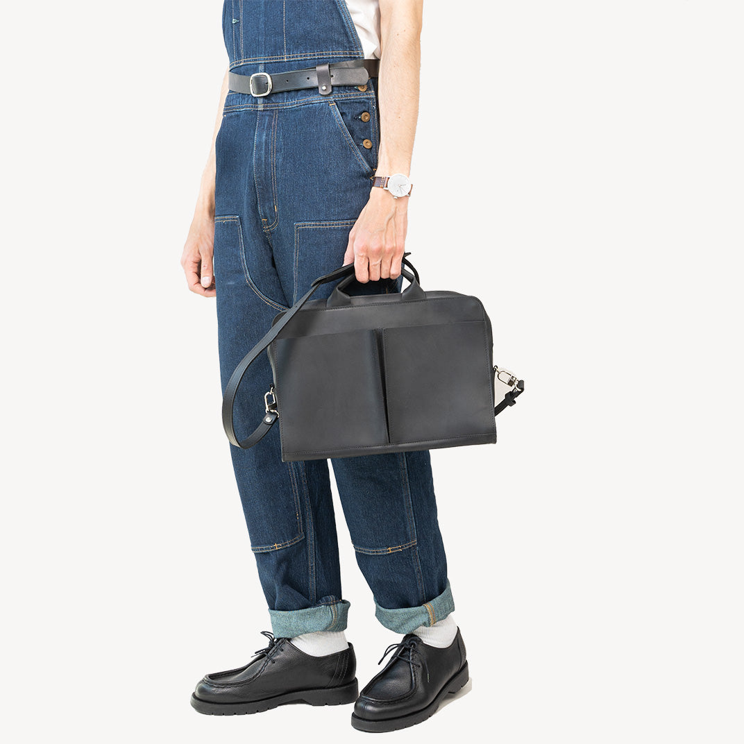 Sac ordinateur en cuir noir porté à la main sur tenue en jean