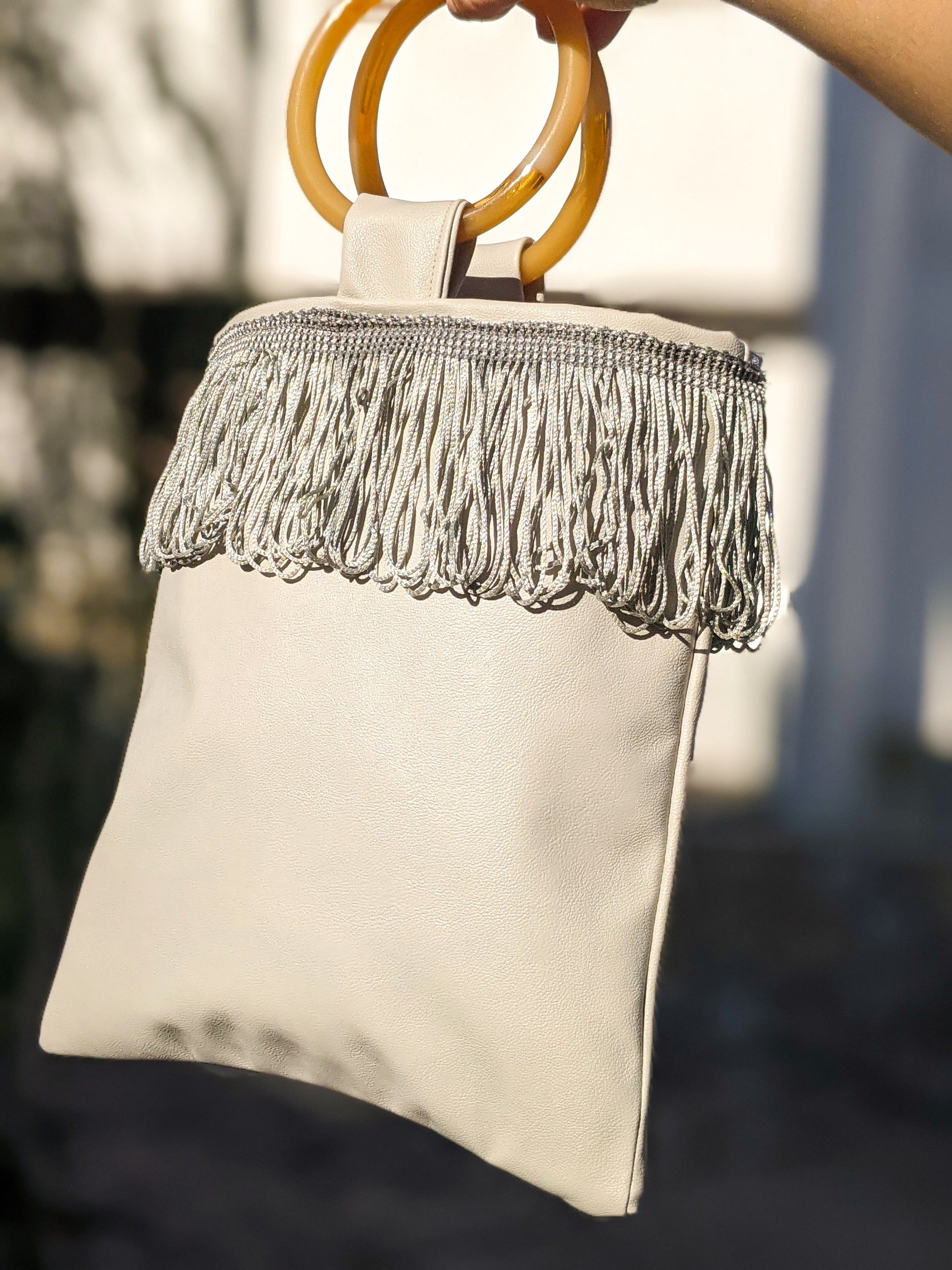 Sac mini simili cuir gris clair, anse anneau orange, franges sur bande supérieure.
