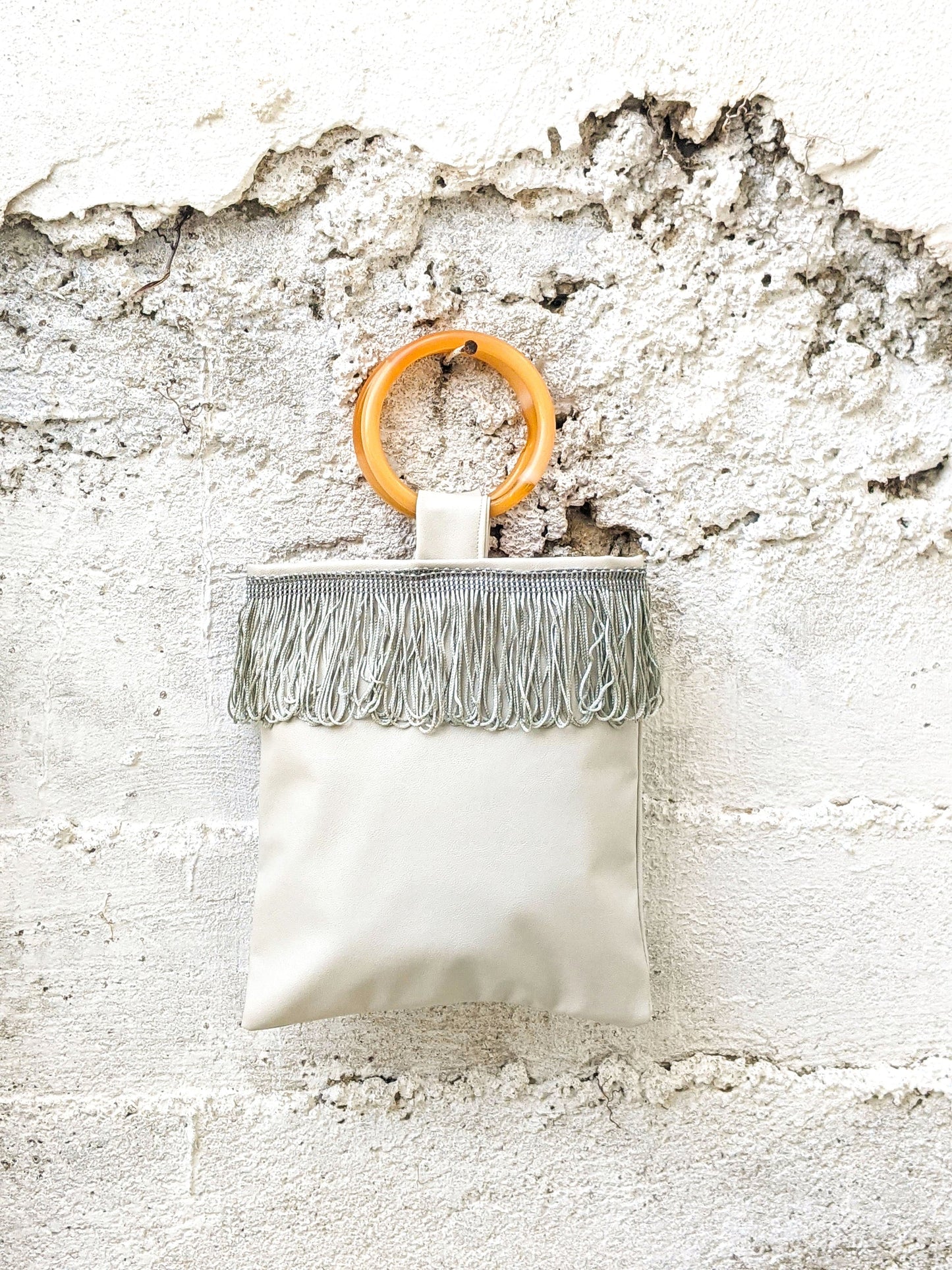 Sac mini en simili cuir gris clair avec anse anneau orange et franges horizontales.