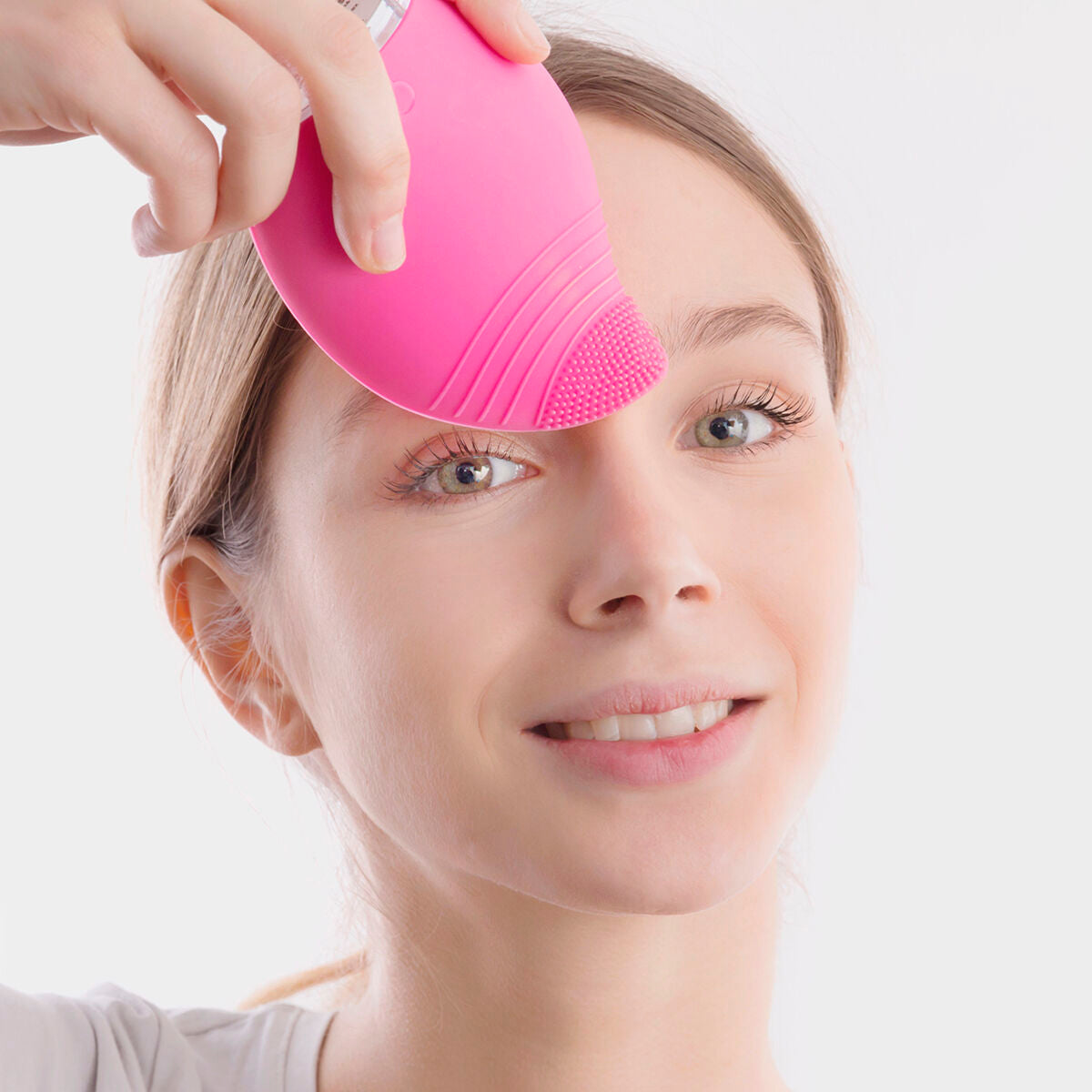Masseur facial rose à picots près de l’œil, main tenant l’appareil contre la peau.