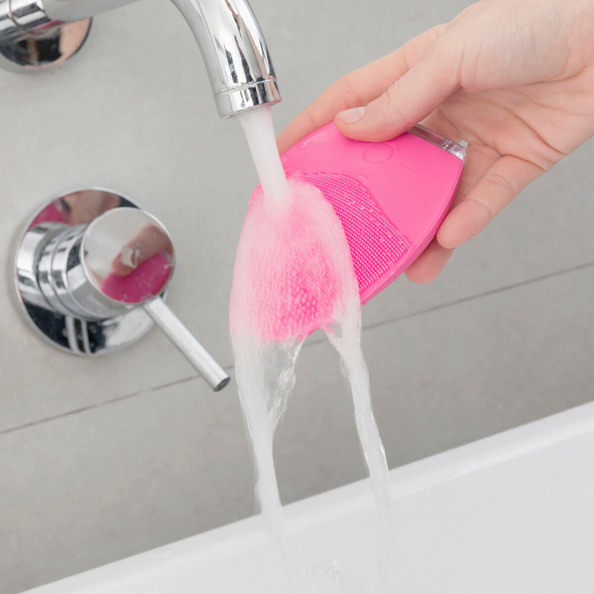 Masseur nettoyant facial rose à picots, eau qui coule pendant l’utilisation.