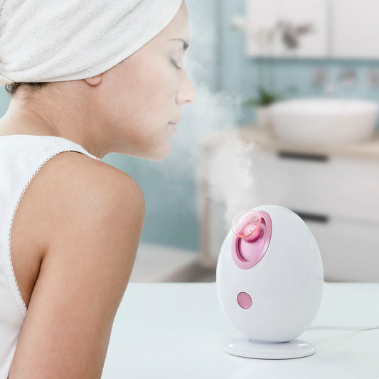 Sauna facial électrique blanc avec buse rose, utilisé avec serviette sur la tête