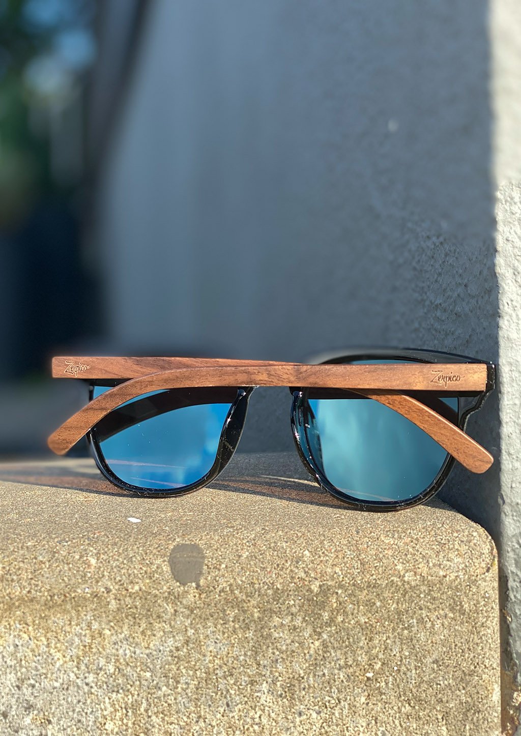 Lunettes de soleil à monture noire, branches en bois et verres bleus.