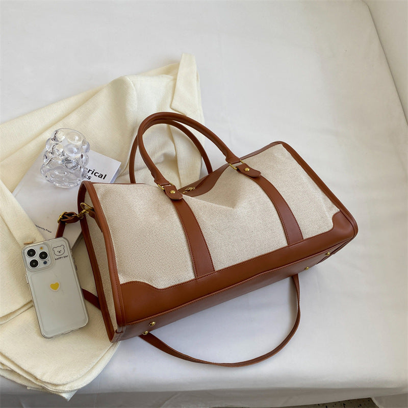 Sac cabas de voyage en toile bicolore posé à plat, bandoulière et poches extérieures