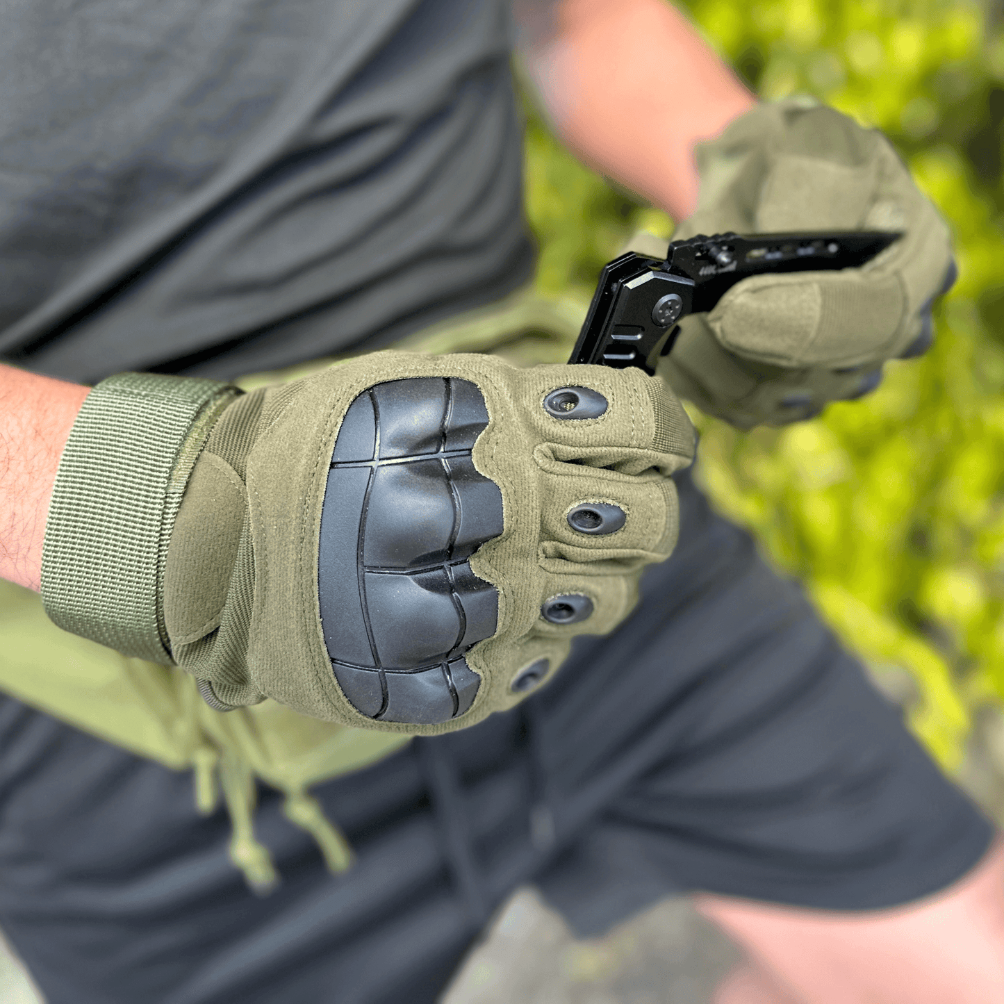 Gants tactiques kaki portés, vue du dos de la main et des protections noires.