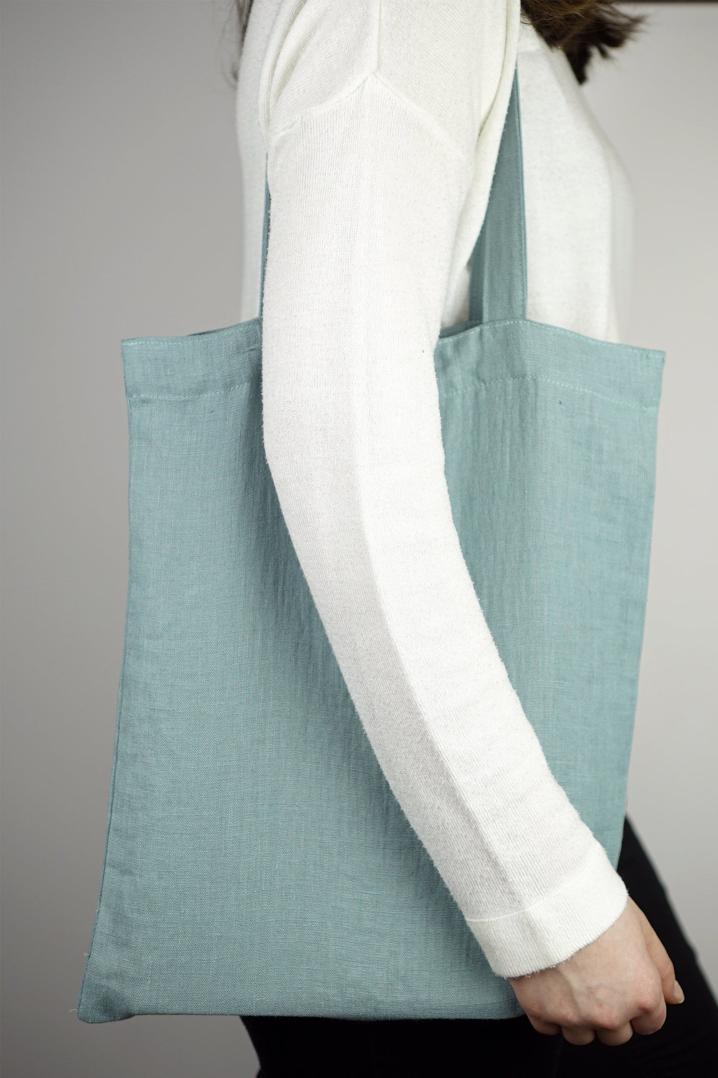 Sac fourre-tout en lin bleu-vert, anses longues, porté sur l’avant-bras.