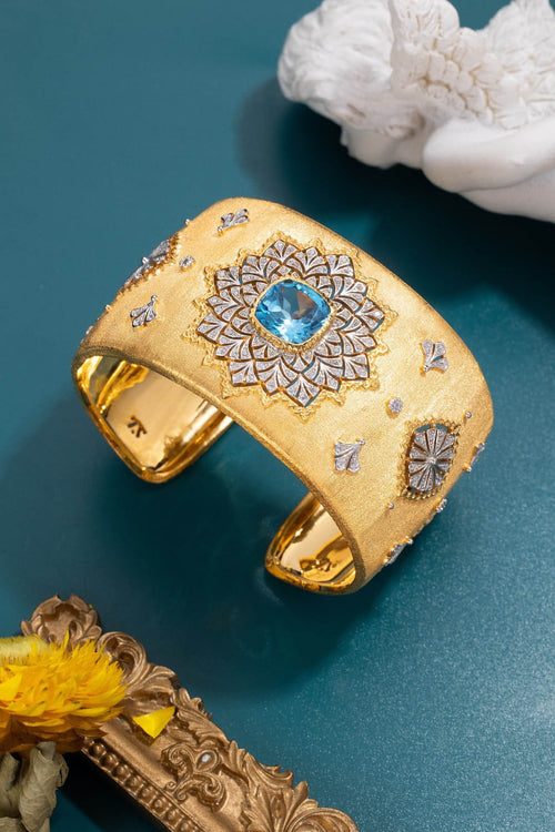 Bracelet manchette doré avec motifs ciselés et pierre bleue au centre, vue de dessus