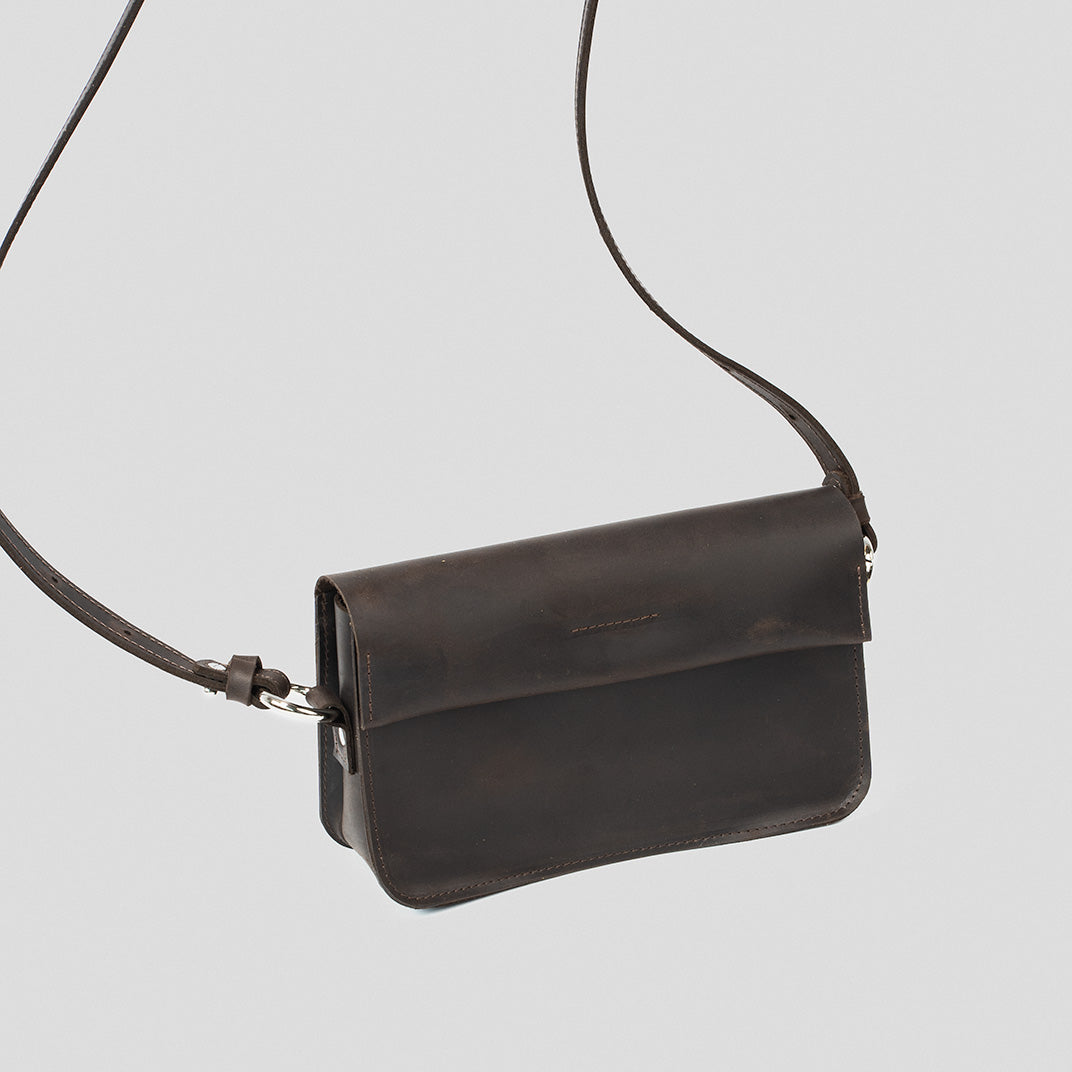 Sac bandoulière en cuir brun foncé, rabat court et fermeture à anneau