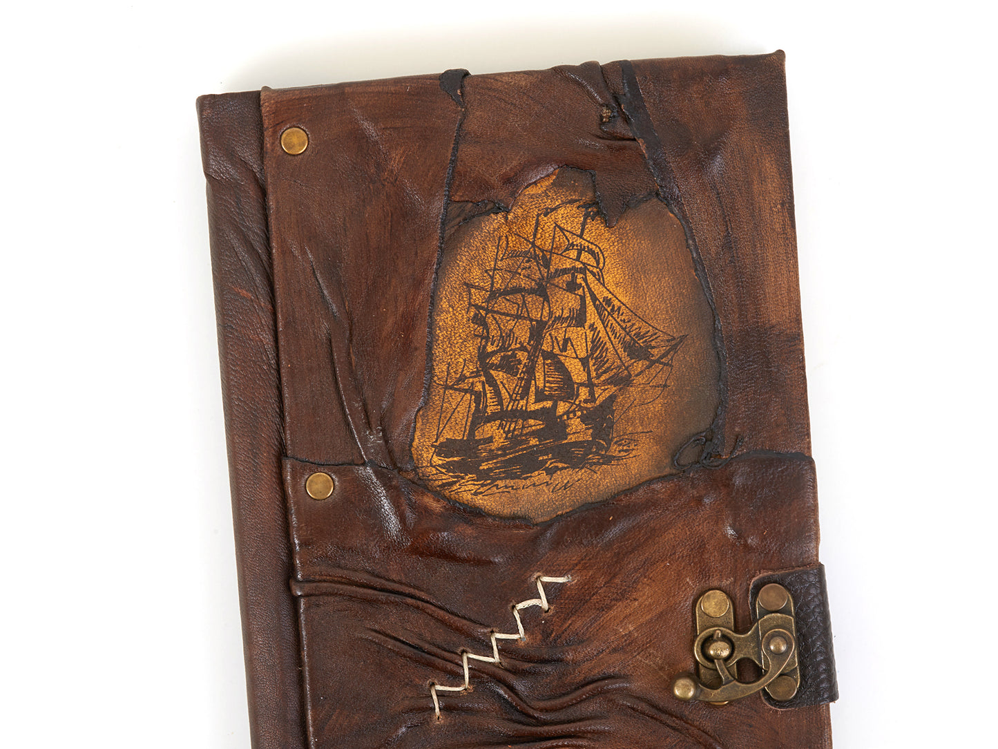 Carnet en cuir brun avec voilier gravé doré, bords cousus et fermoir à lanière.