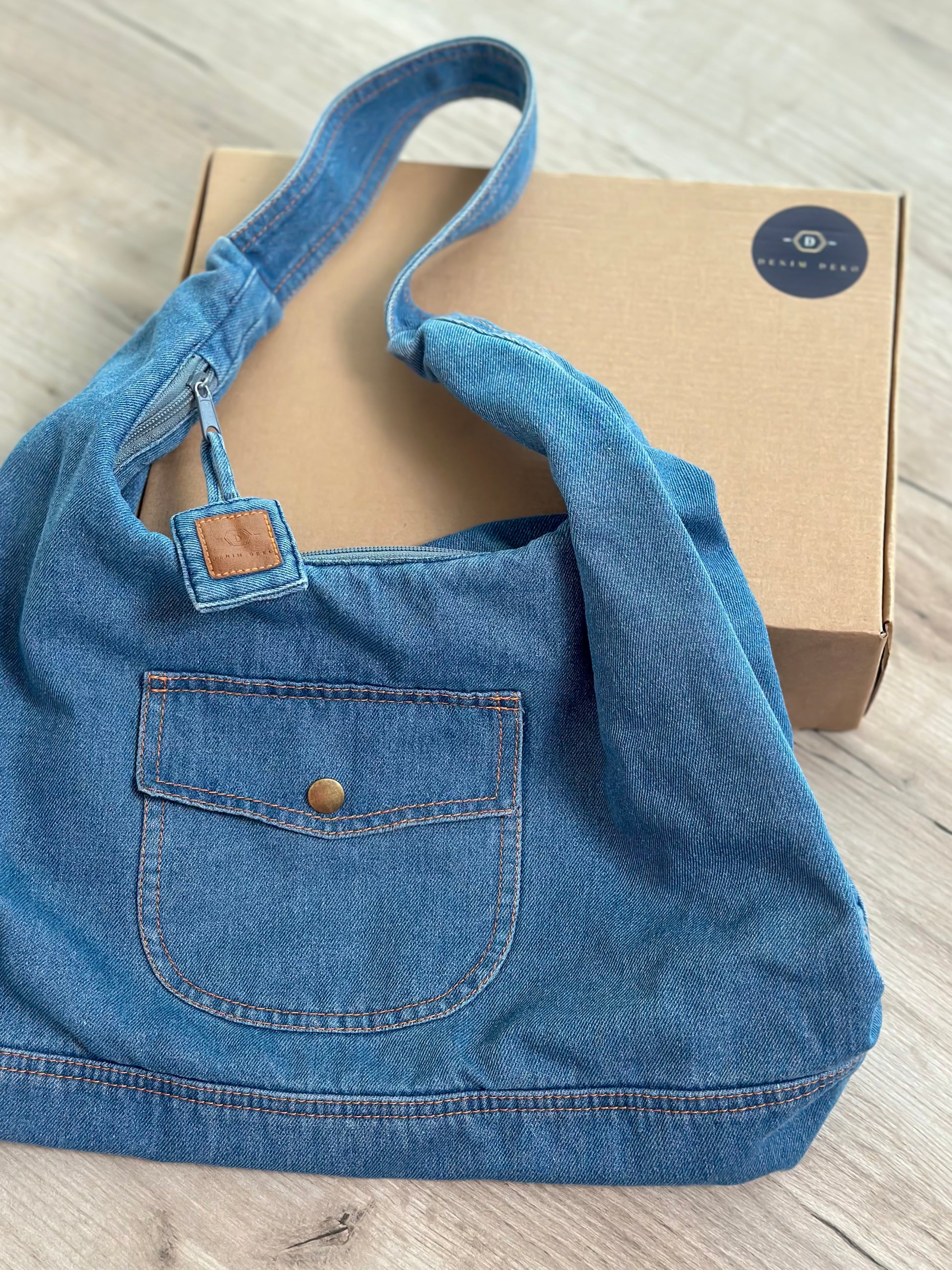Sac hobo en jean bleu clair, anses longues et poche plaquée avec bouton.