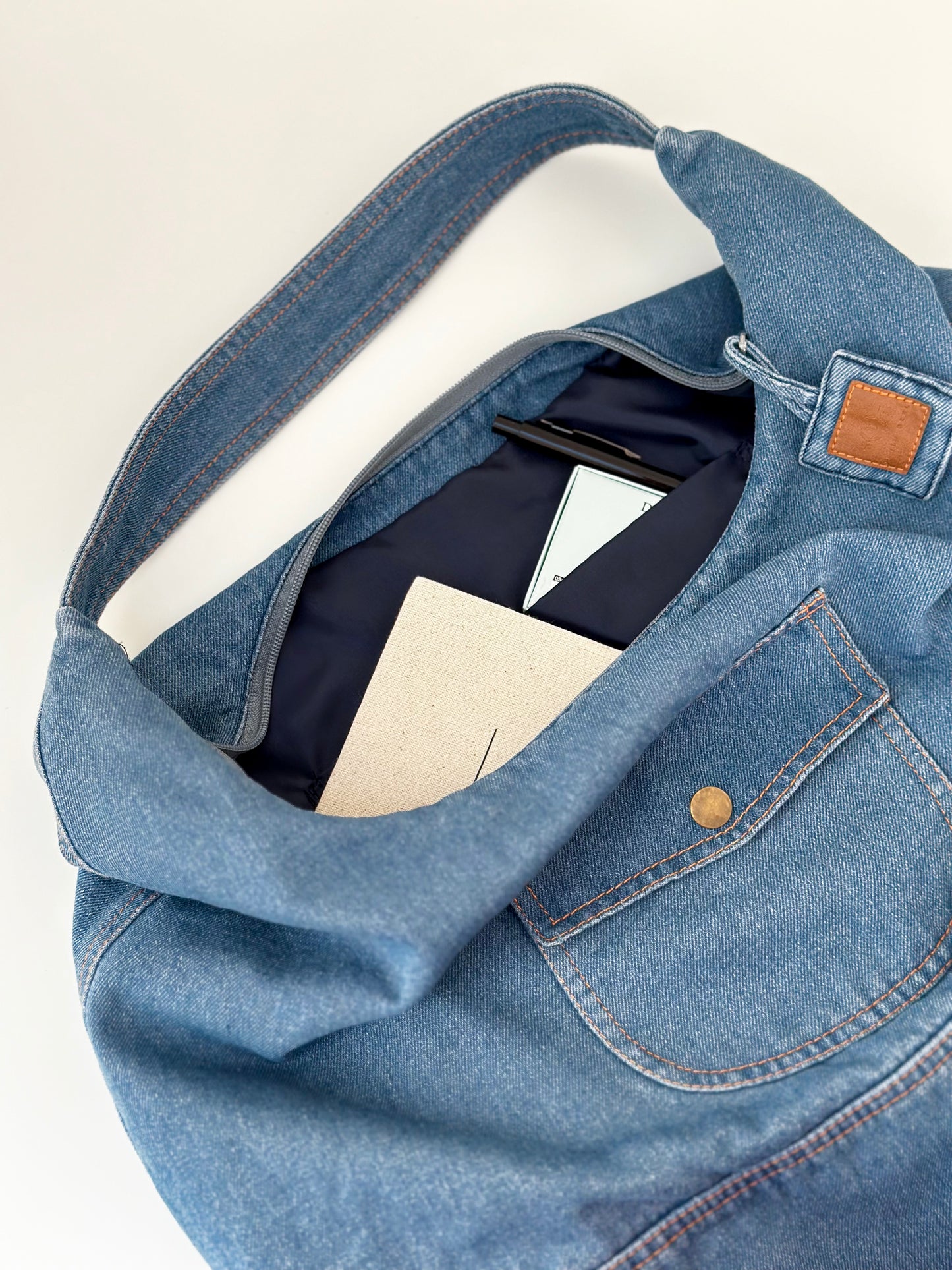 Sac hobo en denim bleu clair, rabat ouvert et poche boutonnée, intérieur visible.