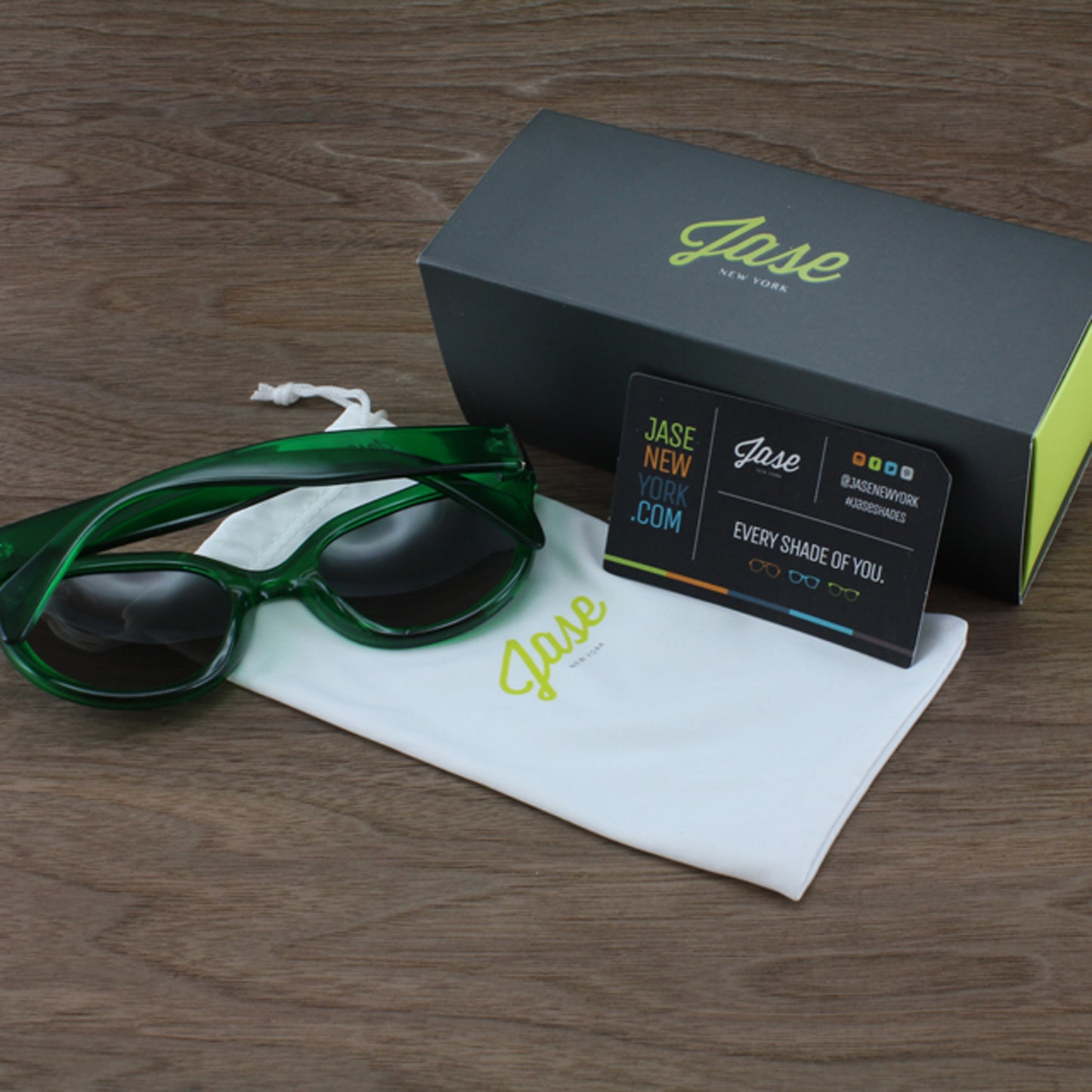 Lunettes de soleil vert émeraude avec étui noir et pochette blanche.