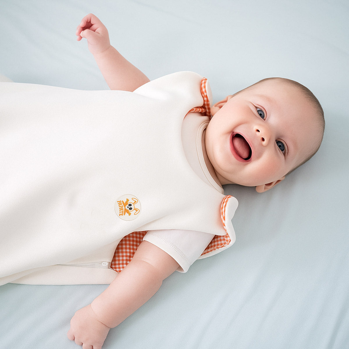 Gigoteuse bébé blanche avec intérieur à carreaux orange, col ouvert et motif brodé.