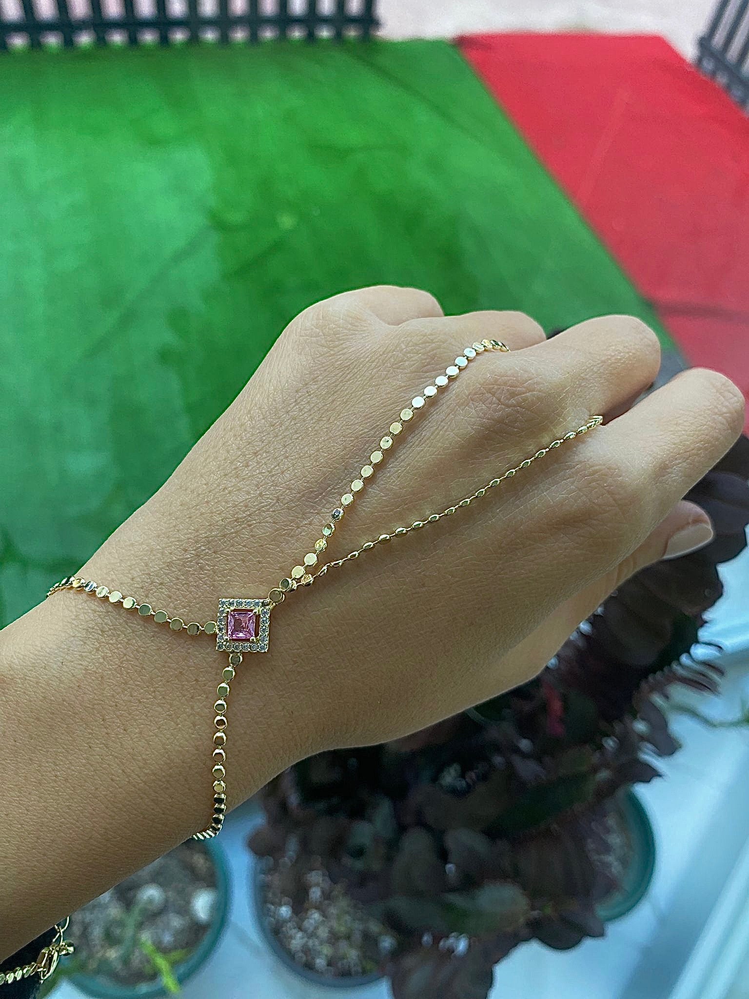 Bracelet fin doré à perles et pendentif carré rose sur le poignet