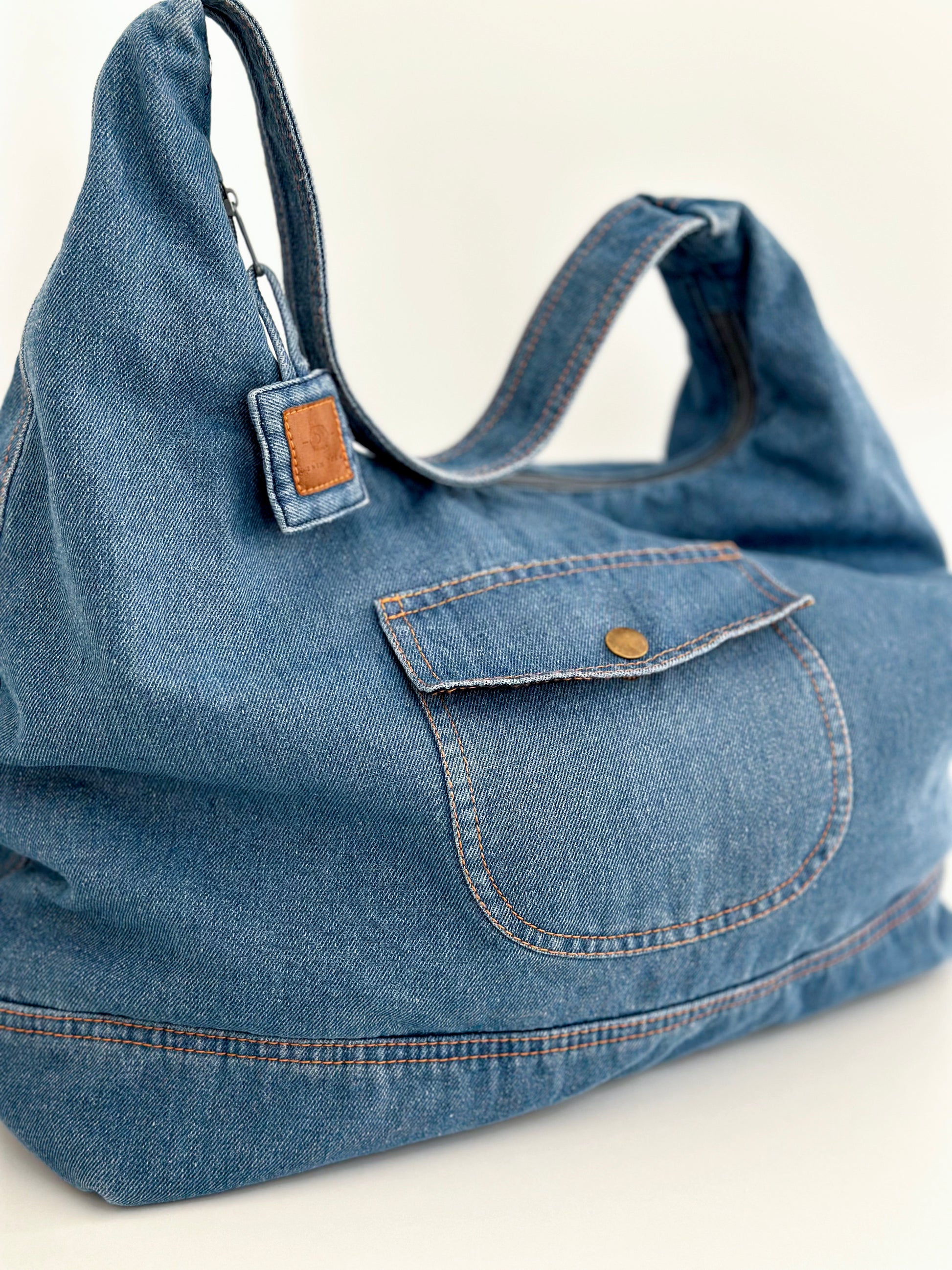 Sac hobo en denim bleu clair, poche frontale boutonnée et surpiqûres visibles.