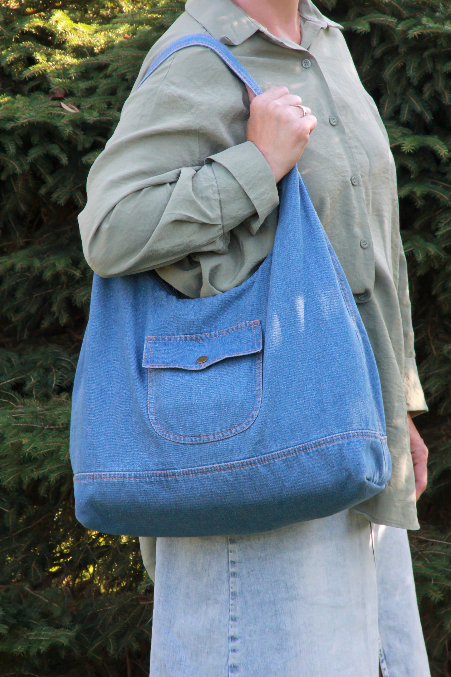Sac hobo en denim bleu clair, poche plaquée et bouton, porté sur l’épaule.