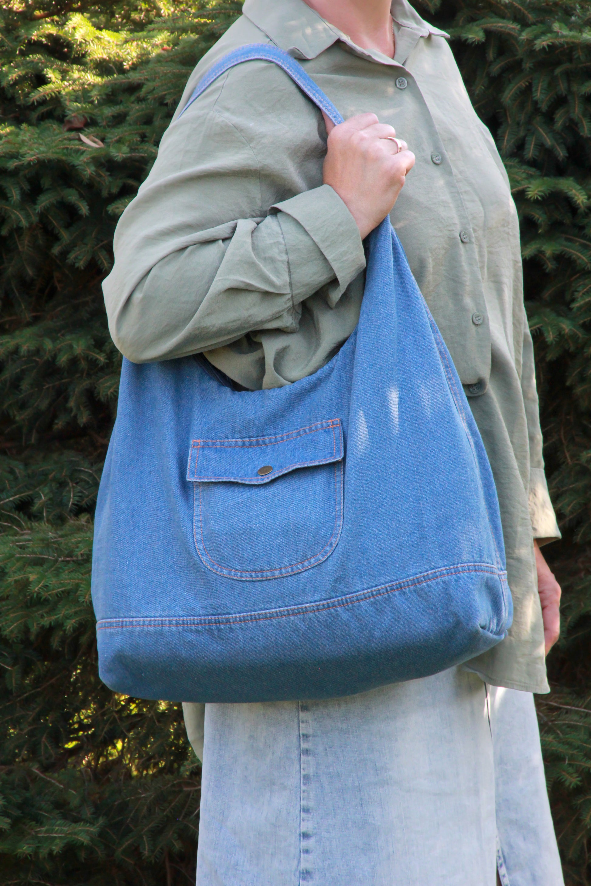 Sac hobo en denim bleu clair, poche plaquée et bouton, porté sur l’épaule.