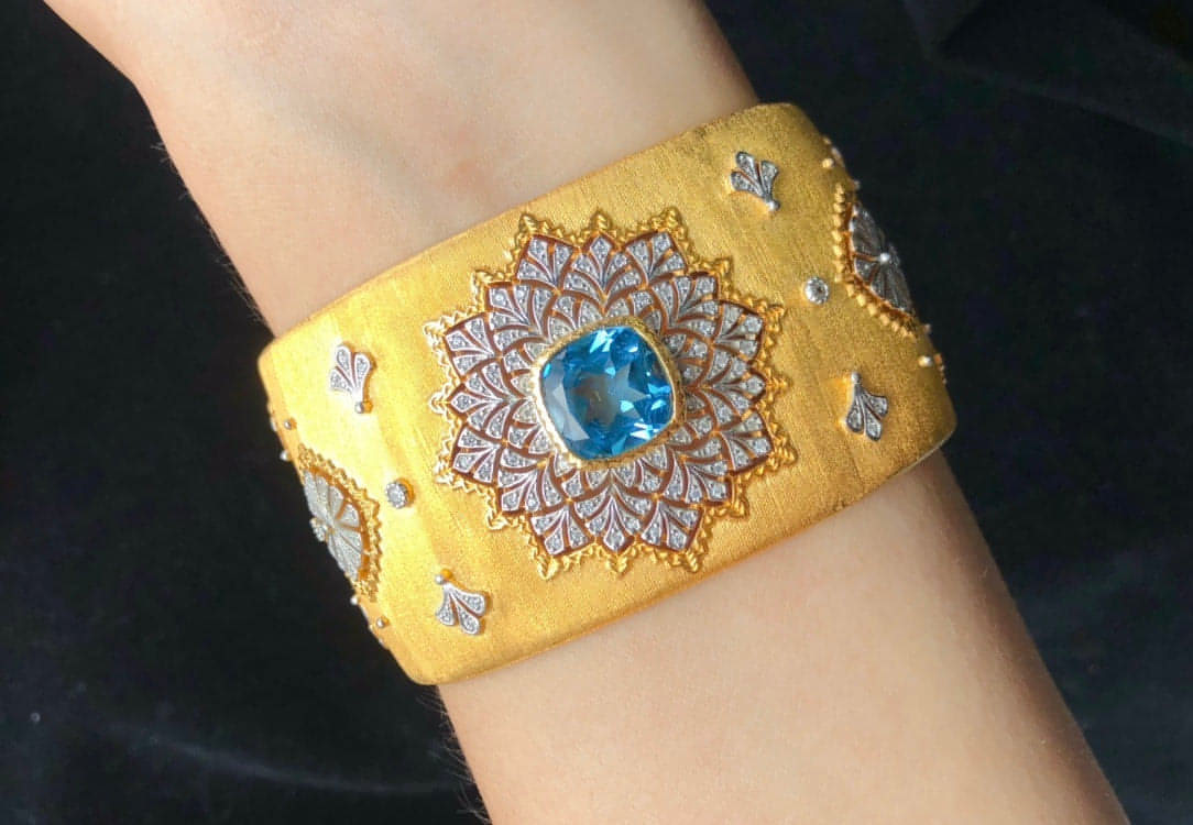 Bracelet manchette doré en gros plan, pierre bleue centrale et cabochons étincelants
