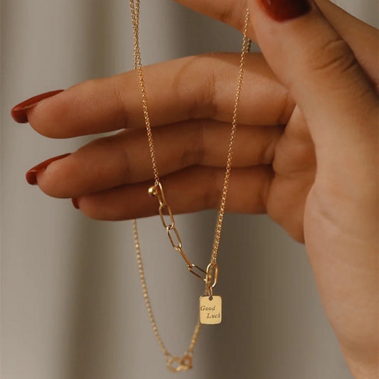 Collier plaqué or à chaîne fine et pendentif carré gravé, porté près de la main