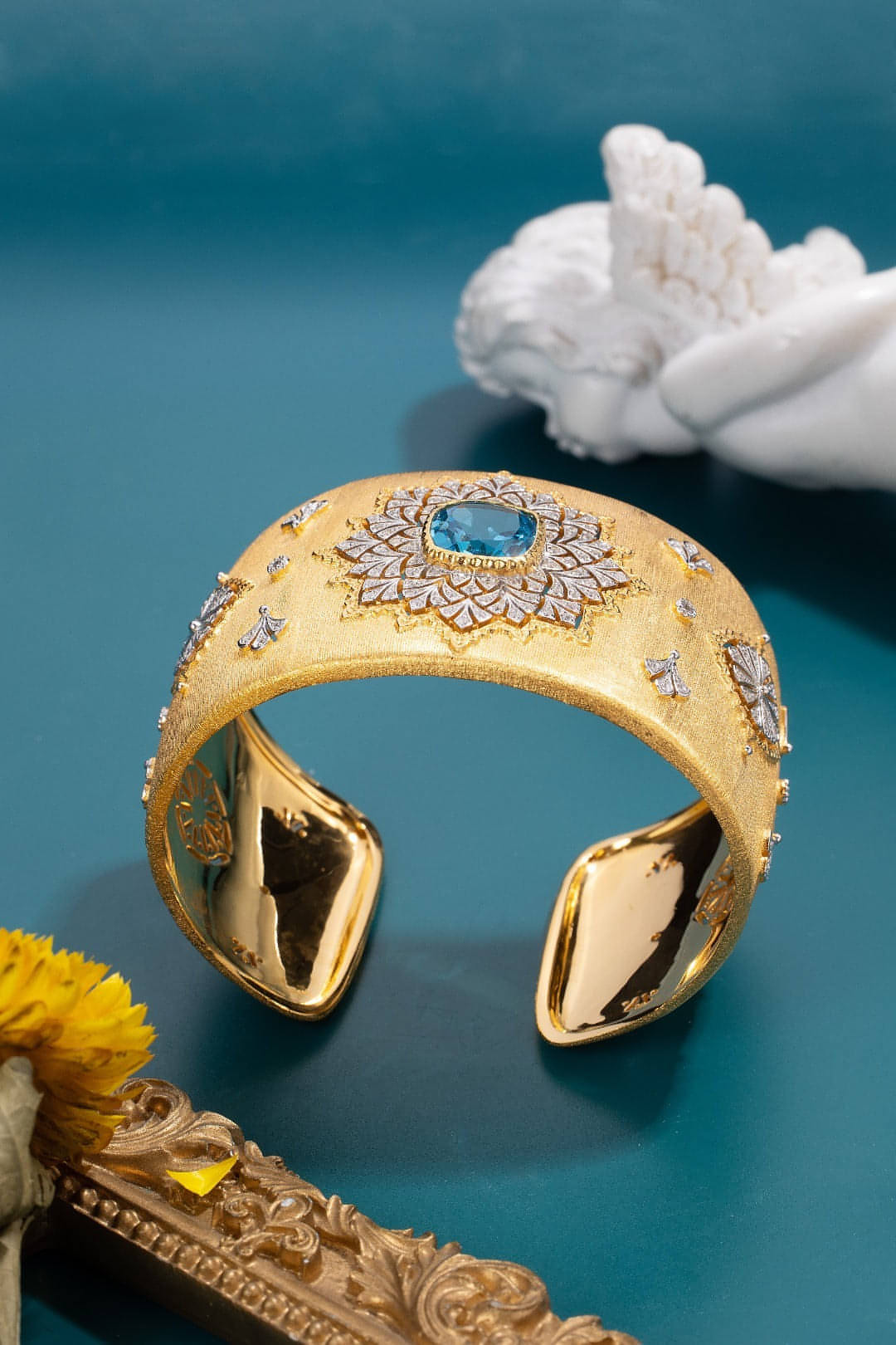 Bracelet manchette doré ouvert, pierre bleue au centre, bord orné de motifs