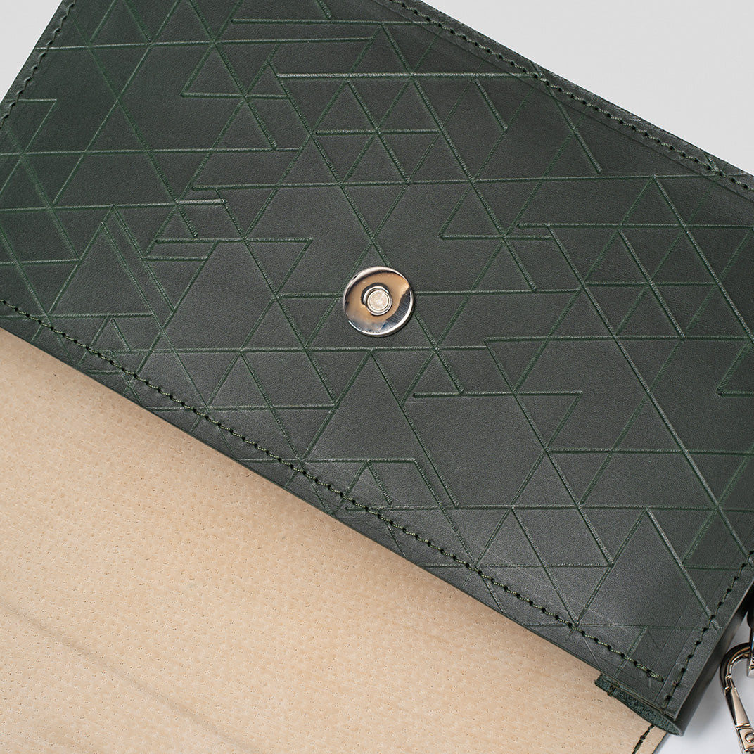 Sac bandoulière cuir vert, doublure à motifs triangulaires et bouton-pression métallique.
