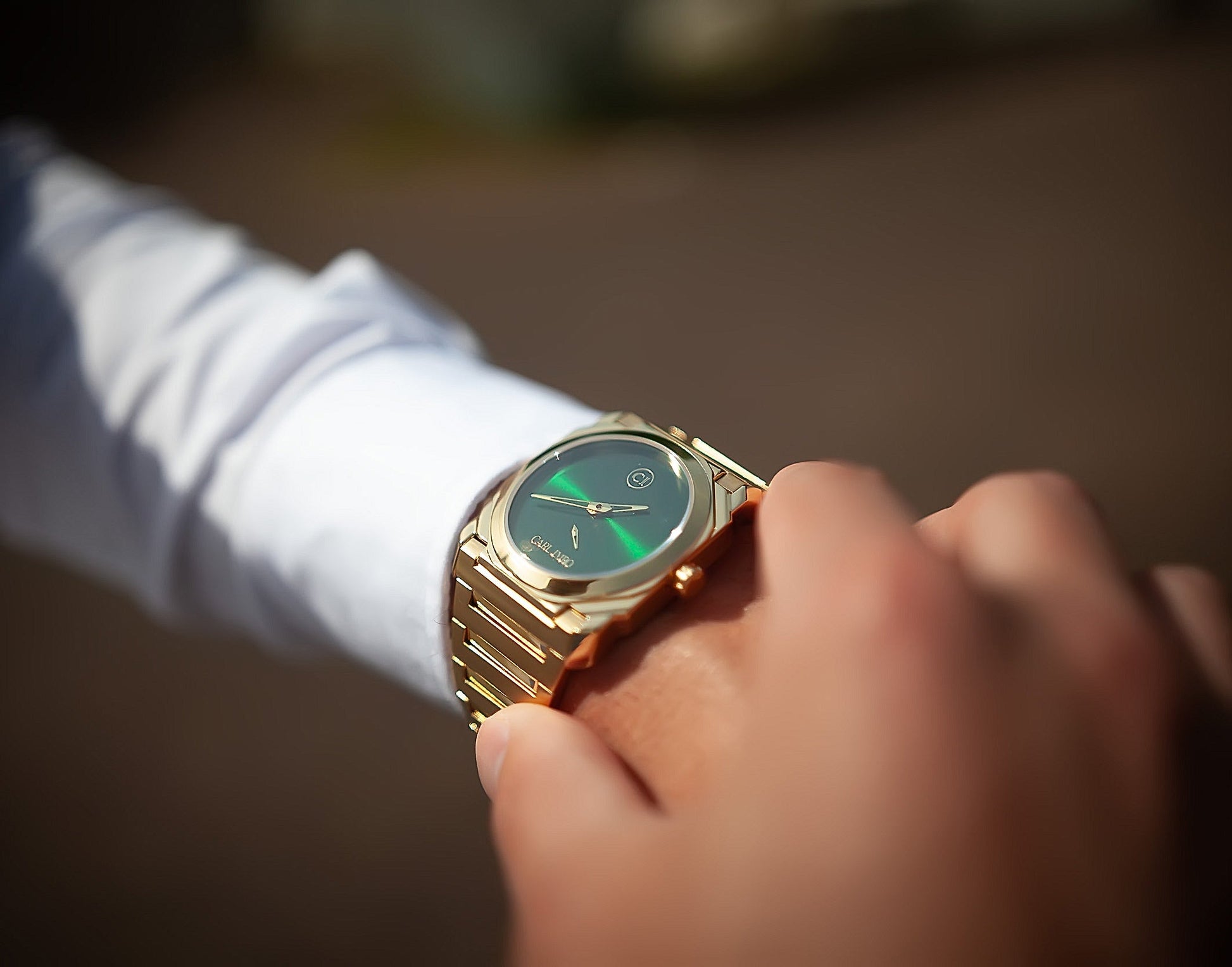 Montre-bracelet homme acier doré, cadran vert, cadran rond, portée à la main.