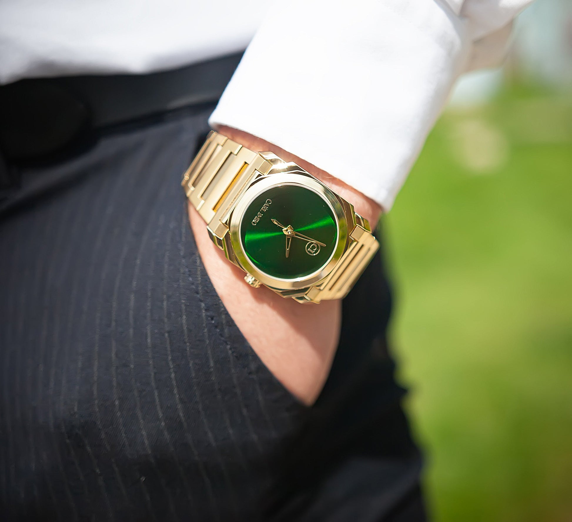 Montre-bracelet en acier doré, cadran vert, portée au poignet avec chemise blanche.