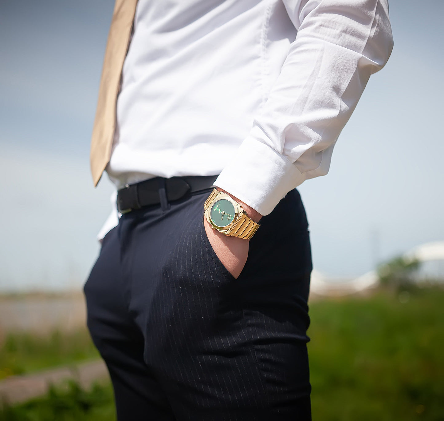 Montre-bracelet homme acier doré, cadran vert, portée sur chemise blanche et pantalon sombre.