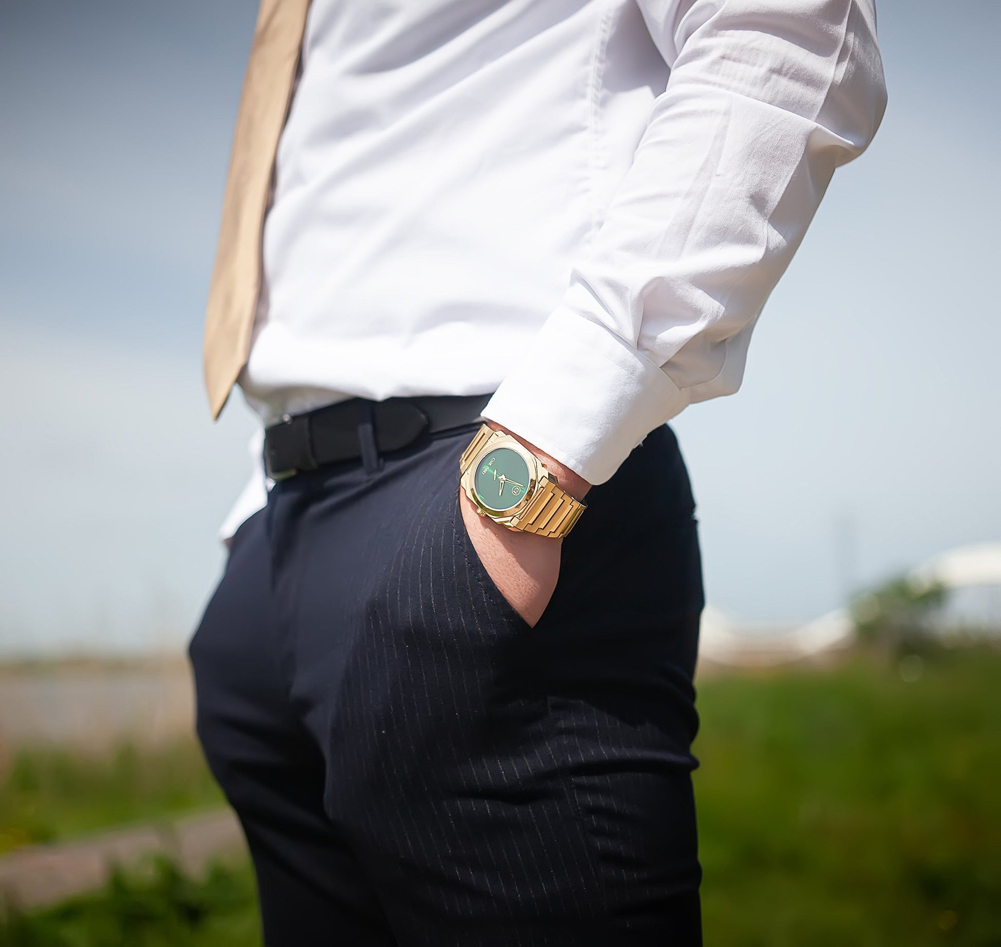 Montre-bracelet homme acier doré, cadran vert, portée sur chemise blanche et pantalon sombre.