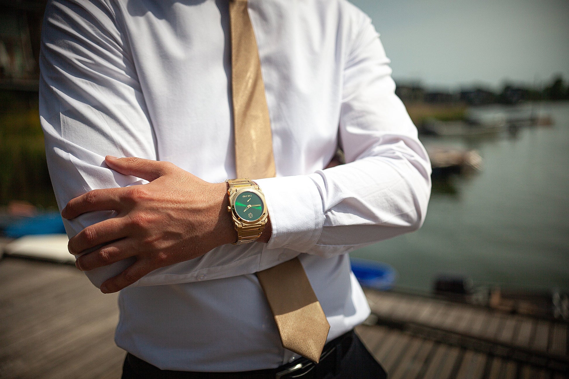 Montre-bracelet homme acier doré avec cadran vert au poignet, portée sur chemise blanche.