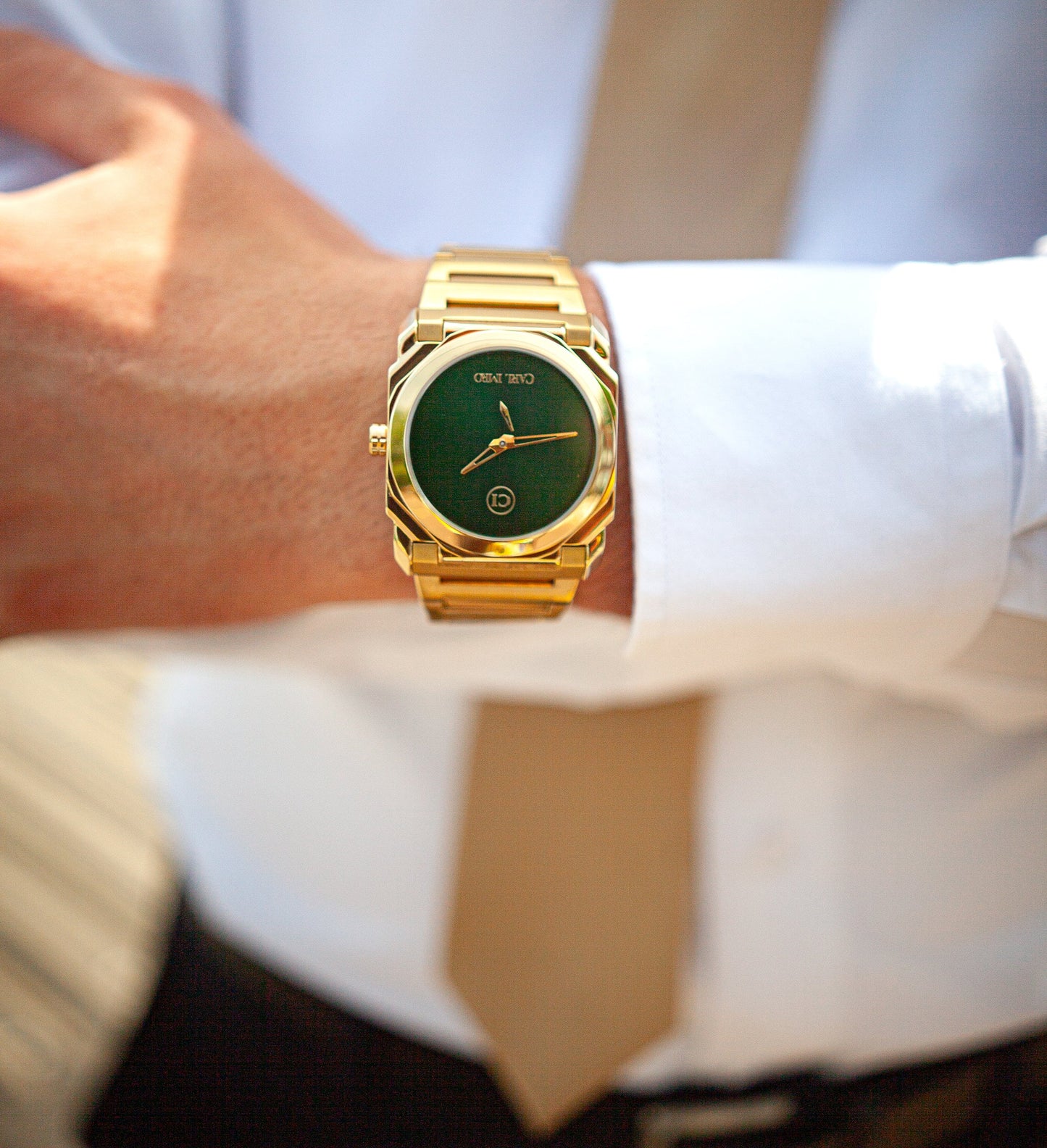 Montre-bracelet acier doré au poignet, cadran vert, chemise blanche et cravate beige.
