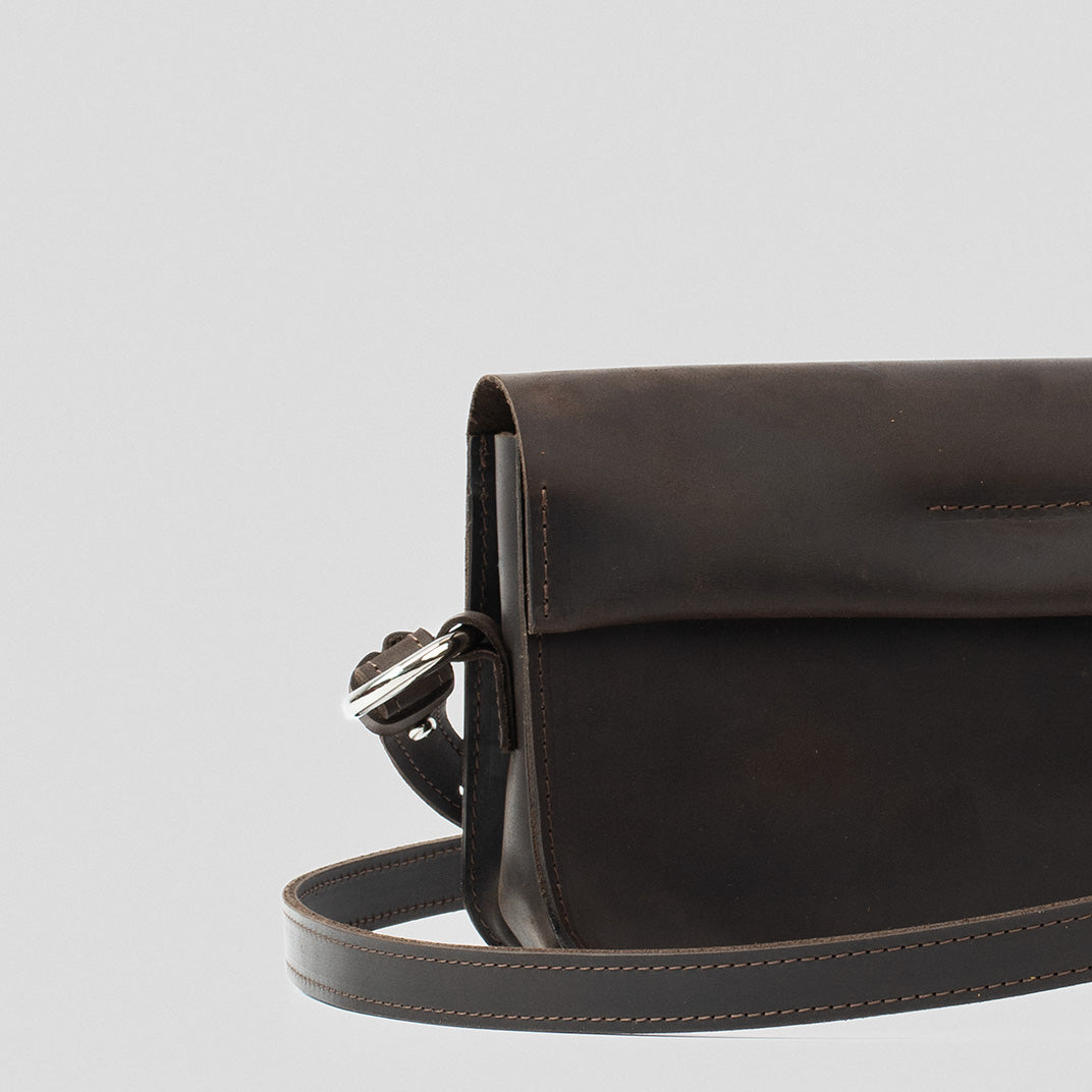 Sac bandoulière en cuir brun foncé, rabat et couture décorative, vue de profil