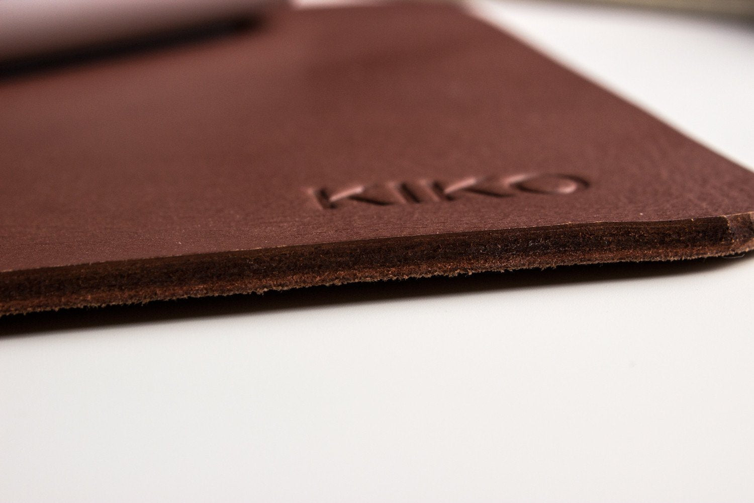 Bord du tapis de souris en cuir brun avec logo KIKO embossé, tranche visible.