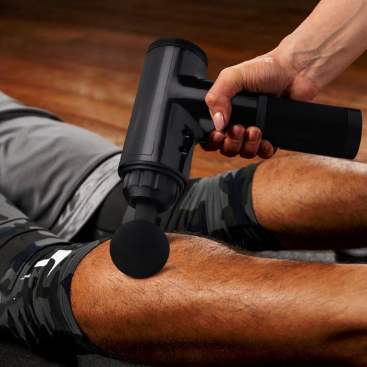 Masseur musculaire portatif noir, tête ronde, utilisé sur la jambe allongée